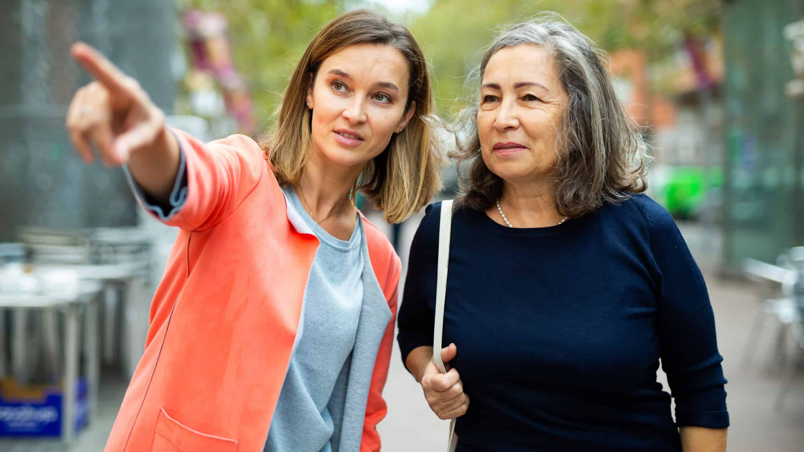 Polite young woman pointing way to aged female tourist on city street on warm autumn day.