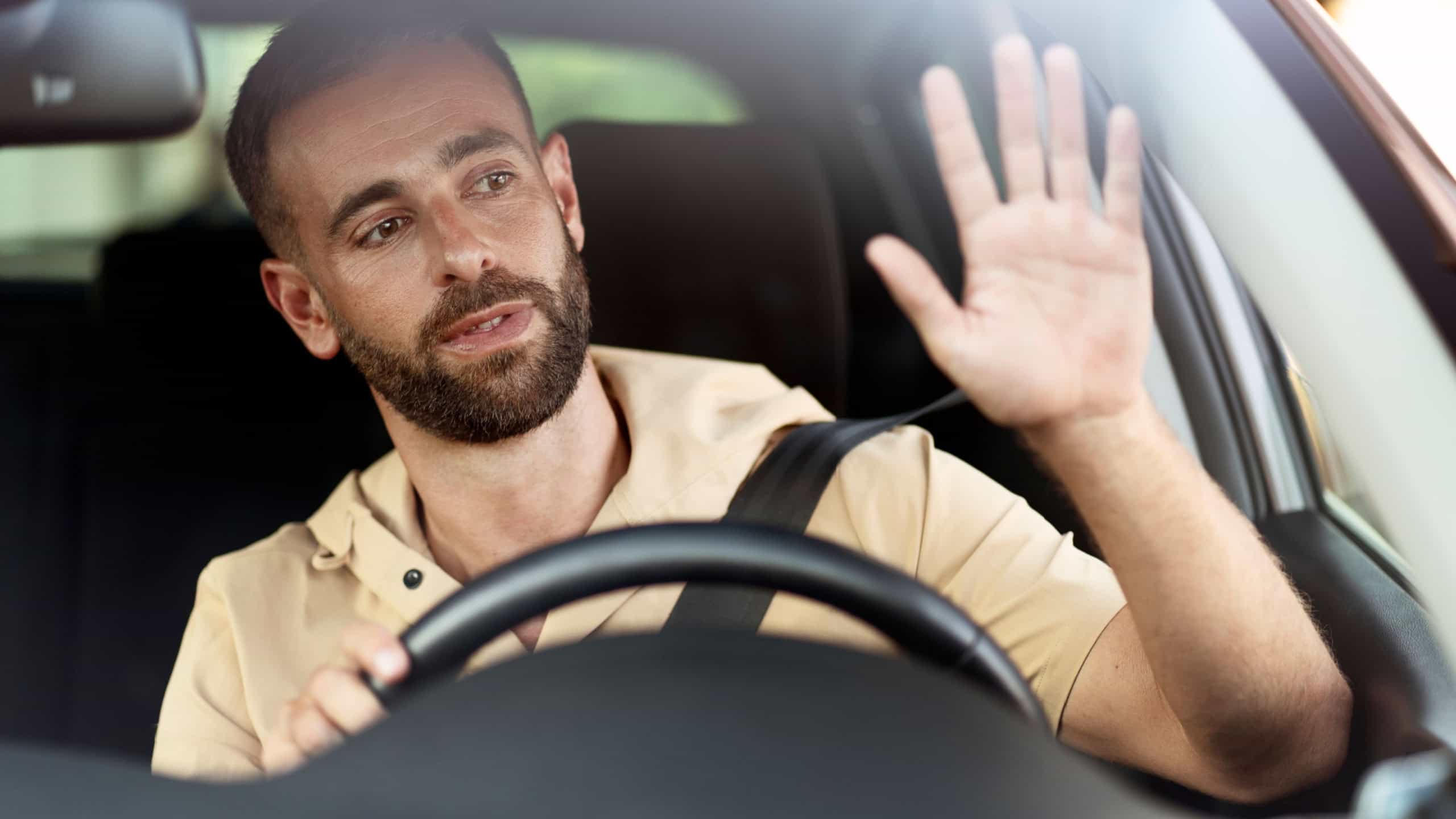 Pensive bearded taxi driver waving hand sitting in car. Transportation concept