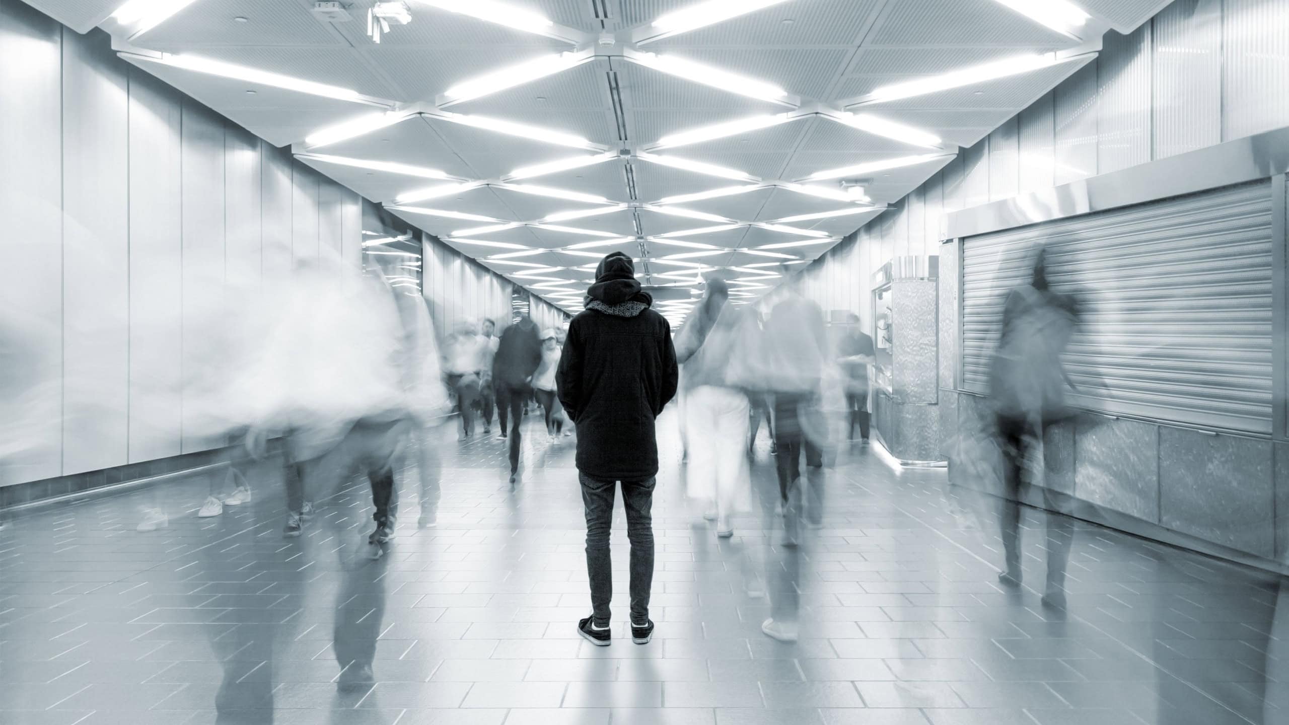 Long exposure picture with lonely man shot from behind at busy walkway with people walking in motion blur, busy city life concept