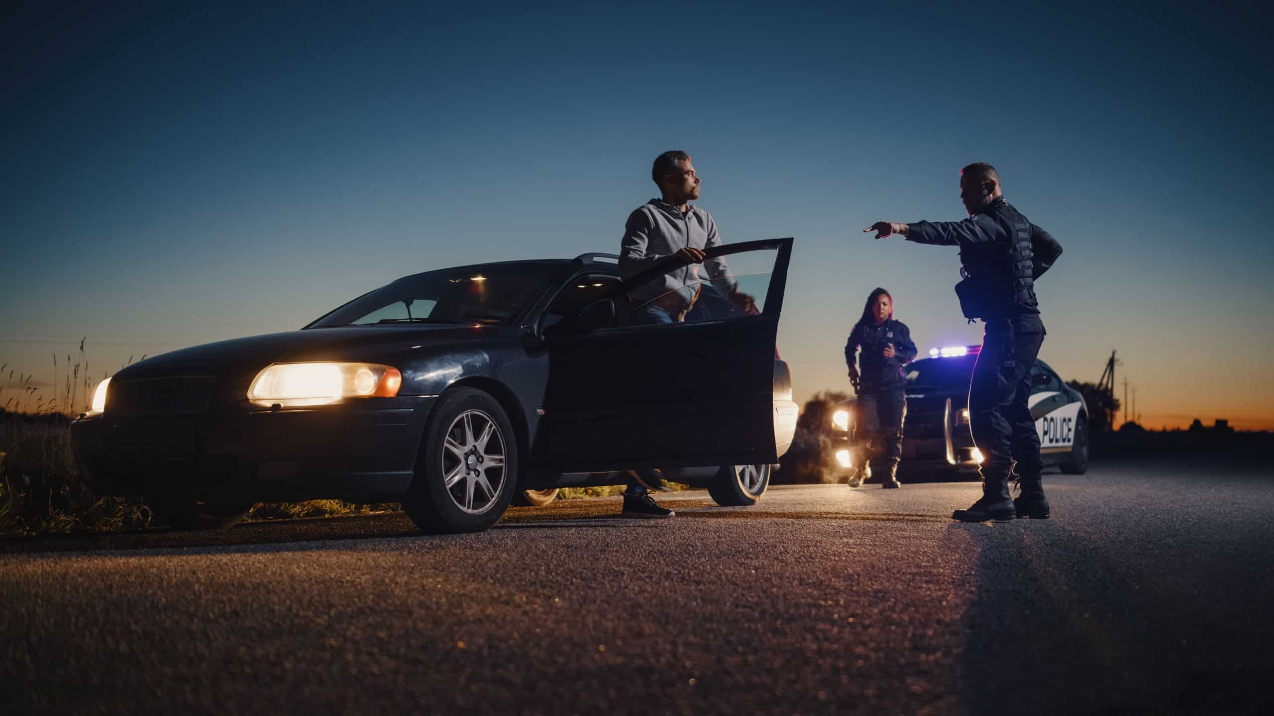 Professional Officer Ordering a Driver to Get Out of the Vehicle and Put His Hands on the Hood of his Car. Female Backup Cop Joins the Scene to Help her Partner. Potentially Fire-Armed Suspect