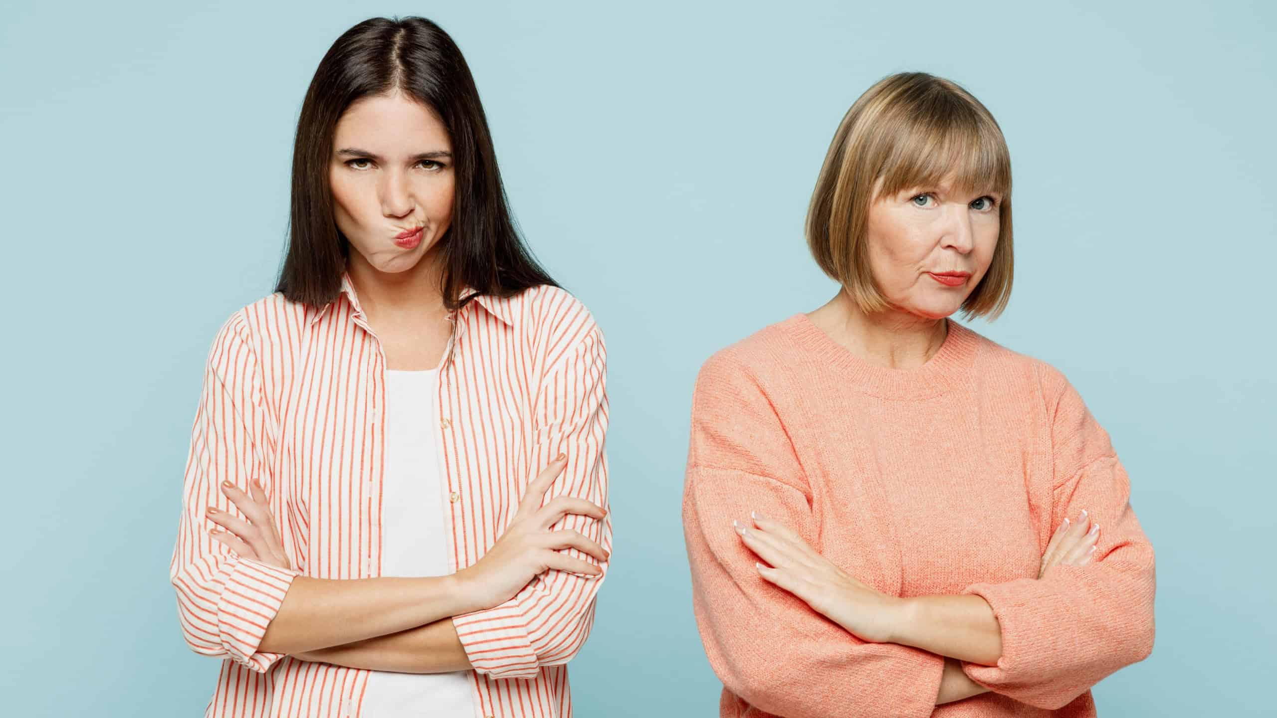 Sad offended miffed elder parent mom with young adult daughter two women together wear casual clothes hold hands crossed folded look camera isolated on plain blue cyan background. Family day concept