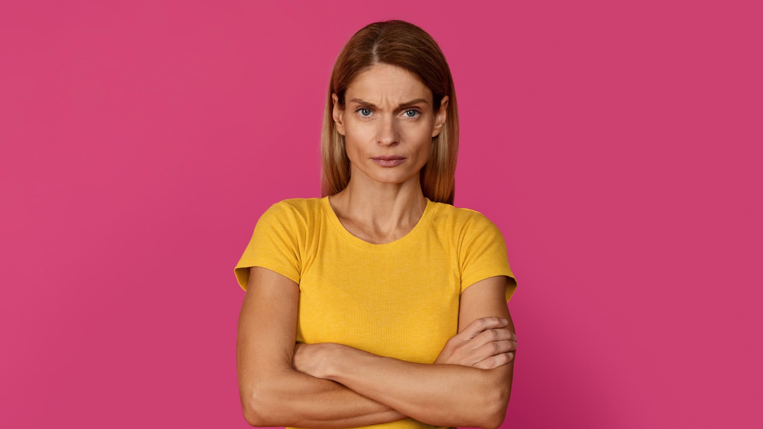 Strict serious angry confident middle aged european blonde lady employee, teacher, professional with crossed arms isolated on pink studio background. People emotions, problems, skeptic