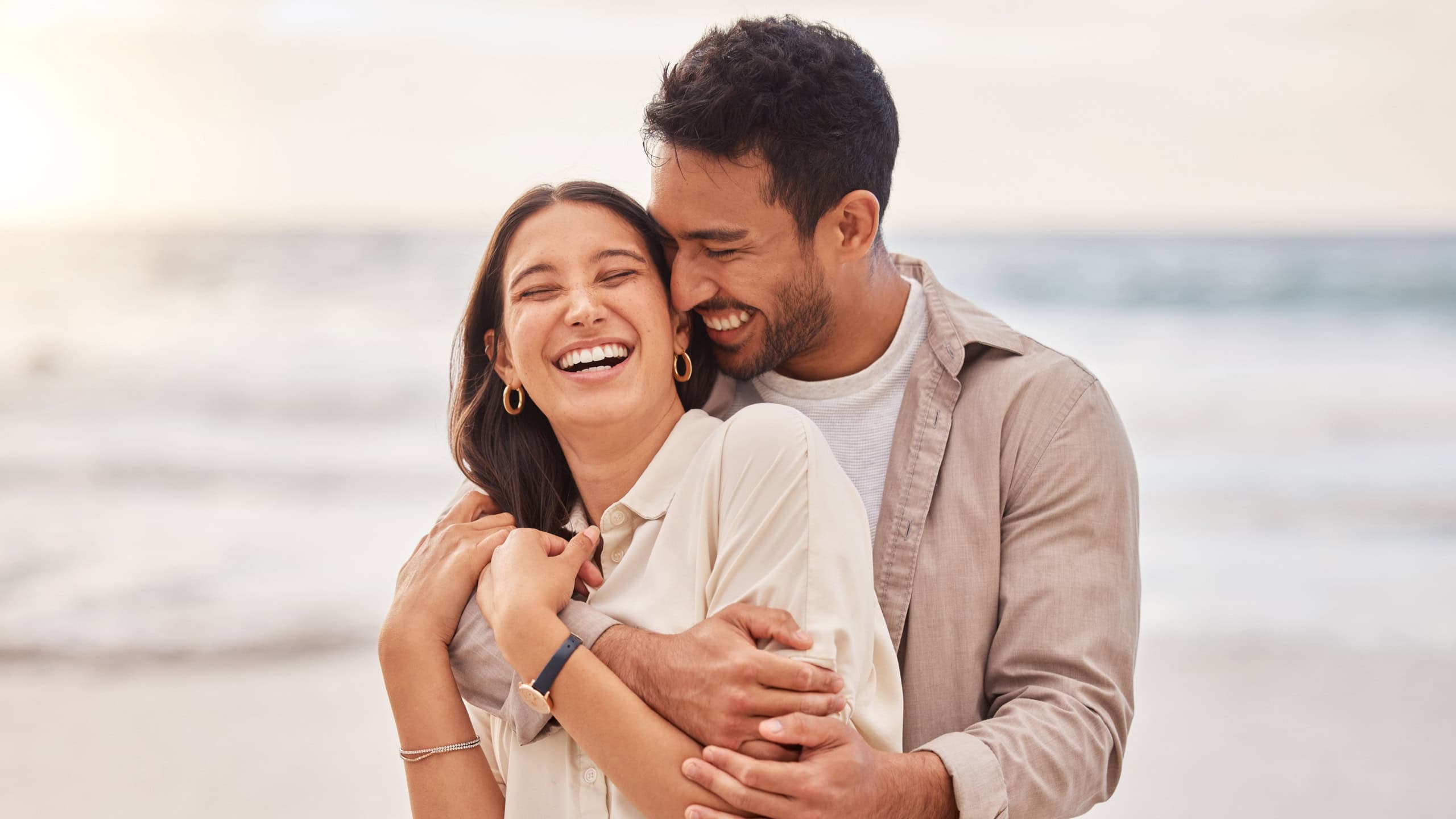 Together, beach and happiness with hug on holiday for having fun with sunset for the weekend. Couple, vacation and laughing with face at the ocean for travel in the summer for a relaxing time.