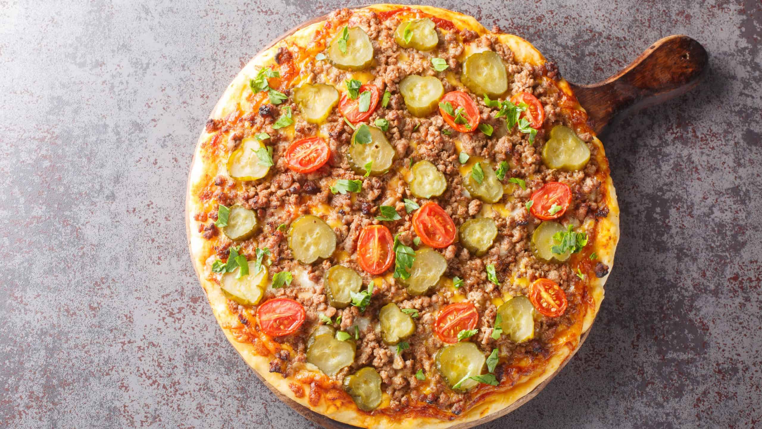 Tasty Pizza is topped with a creamy burger sauce, ground beef, cheese and pickles closeup on the wooden board on the table. Horizontal top view from above