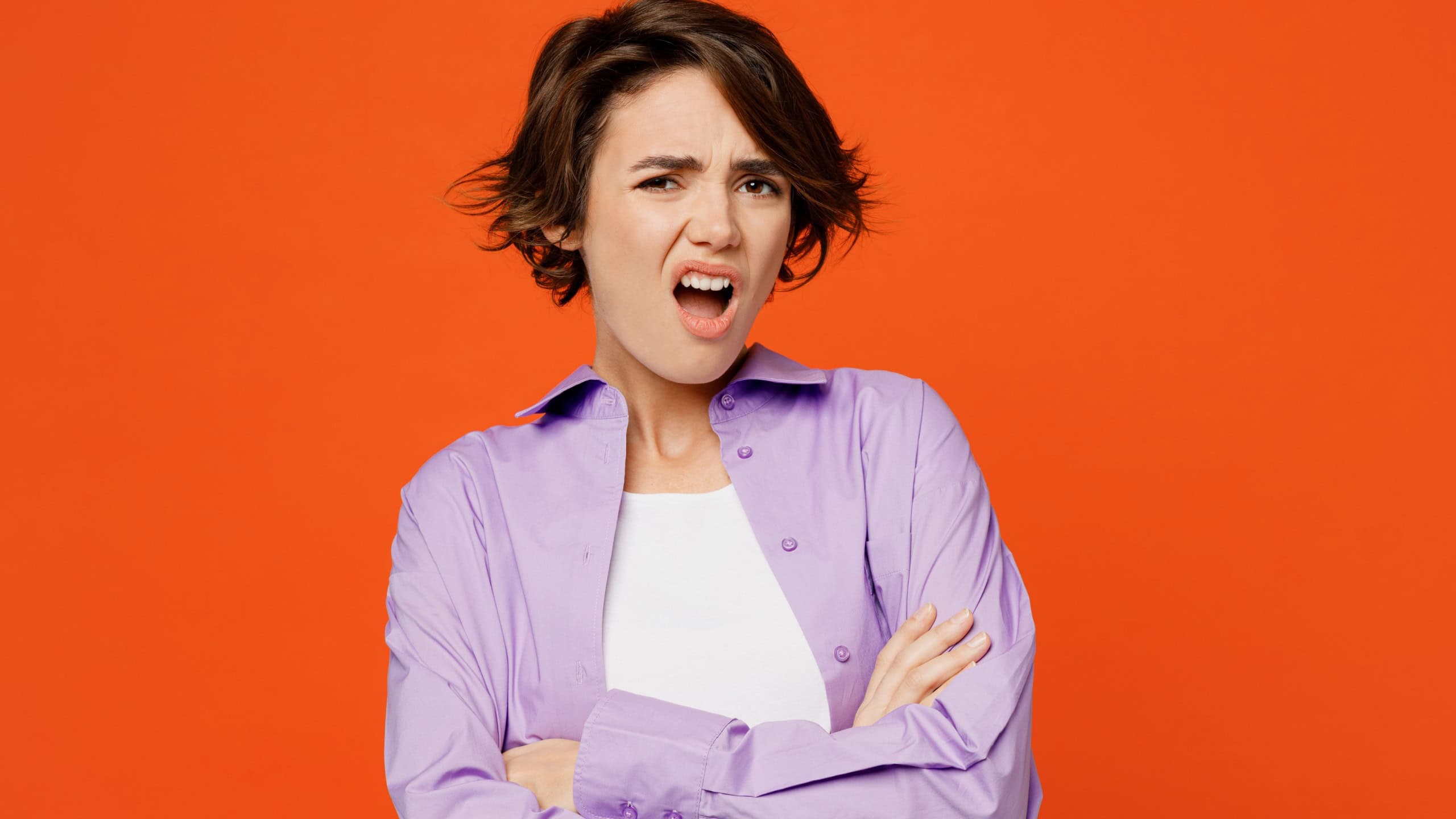 Young irritated indignant annoyed sad caucasian woman she wearing purple shirt white t-shirt casual clothes hold hands crossed isolated on plain orange background studio portrait. Lifestyle concept