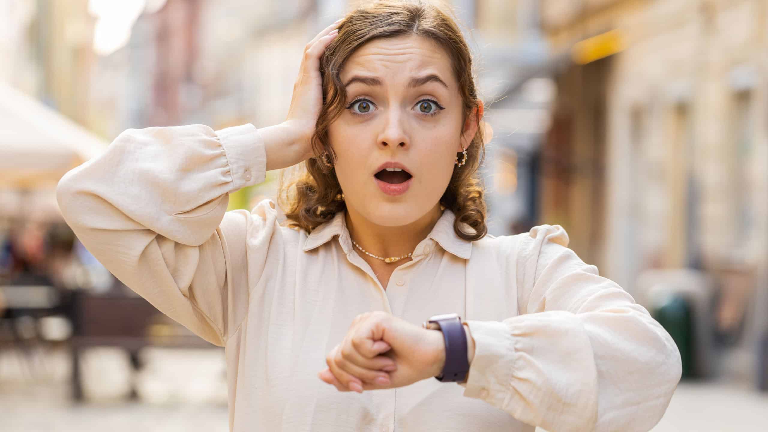 Scared woman worrying to be punctual, with anxiety checking time on watch, running late to work or transport, being in delay, deadline outdoors. Girl tourist walking in city street. Town lifestyles