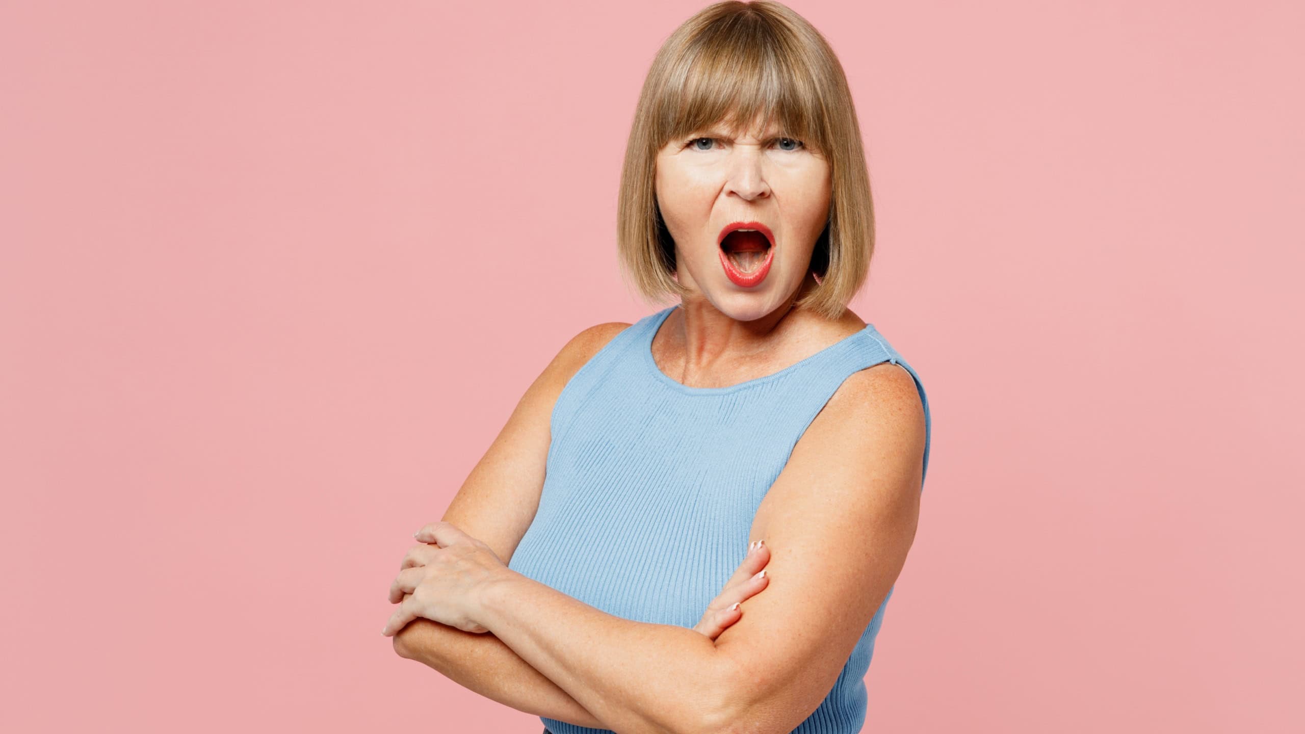 Side view elderly sad blonde woman 50s years old she wears blue undershirt casual clothes look camera hold hands crossed folded scream isolated on plain pastel light pink background. Lifestyle concept