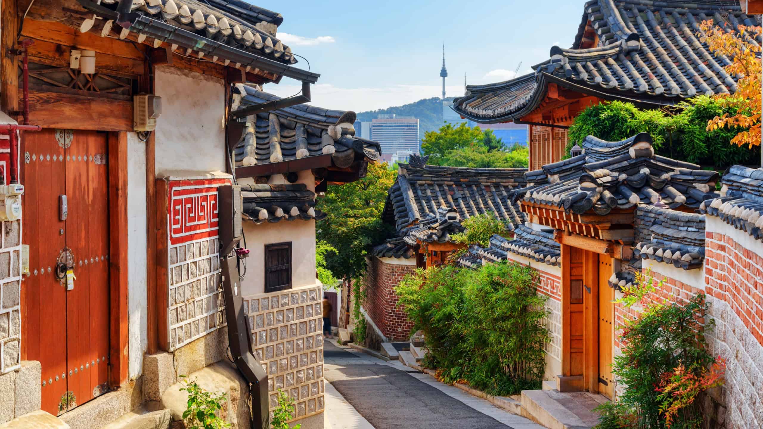 Gorgeous view of cozy old narrow street and traditional Korean houses of Bukchon Hanok Village in Seoul, South Korea. Seoul Tower on Namsan Mountain is visible on blue sky background. Scenic cityscape
