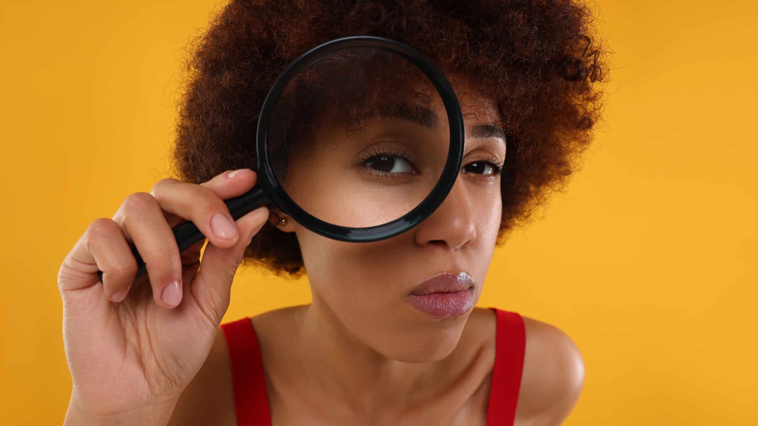 Young woman looking through magnifier glass on orange background