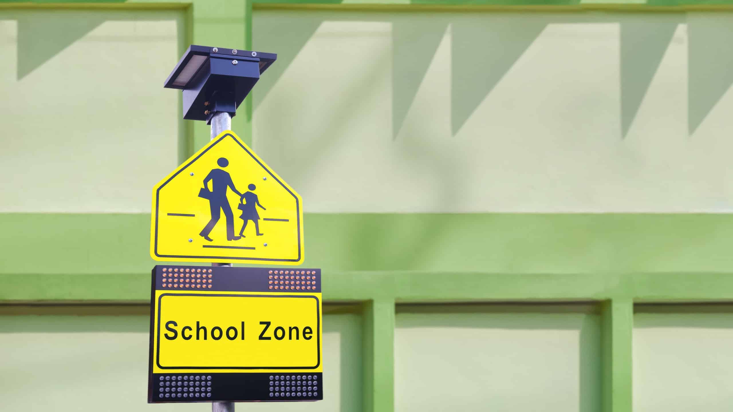 LED solar cell warning flashing orange light with traffic security school sign on metal signpost with blurred school building wall background
