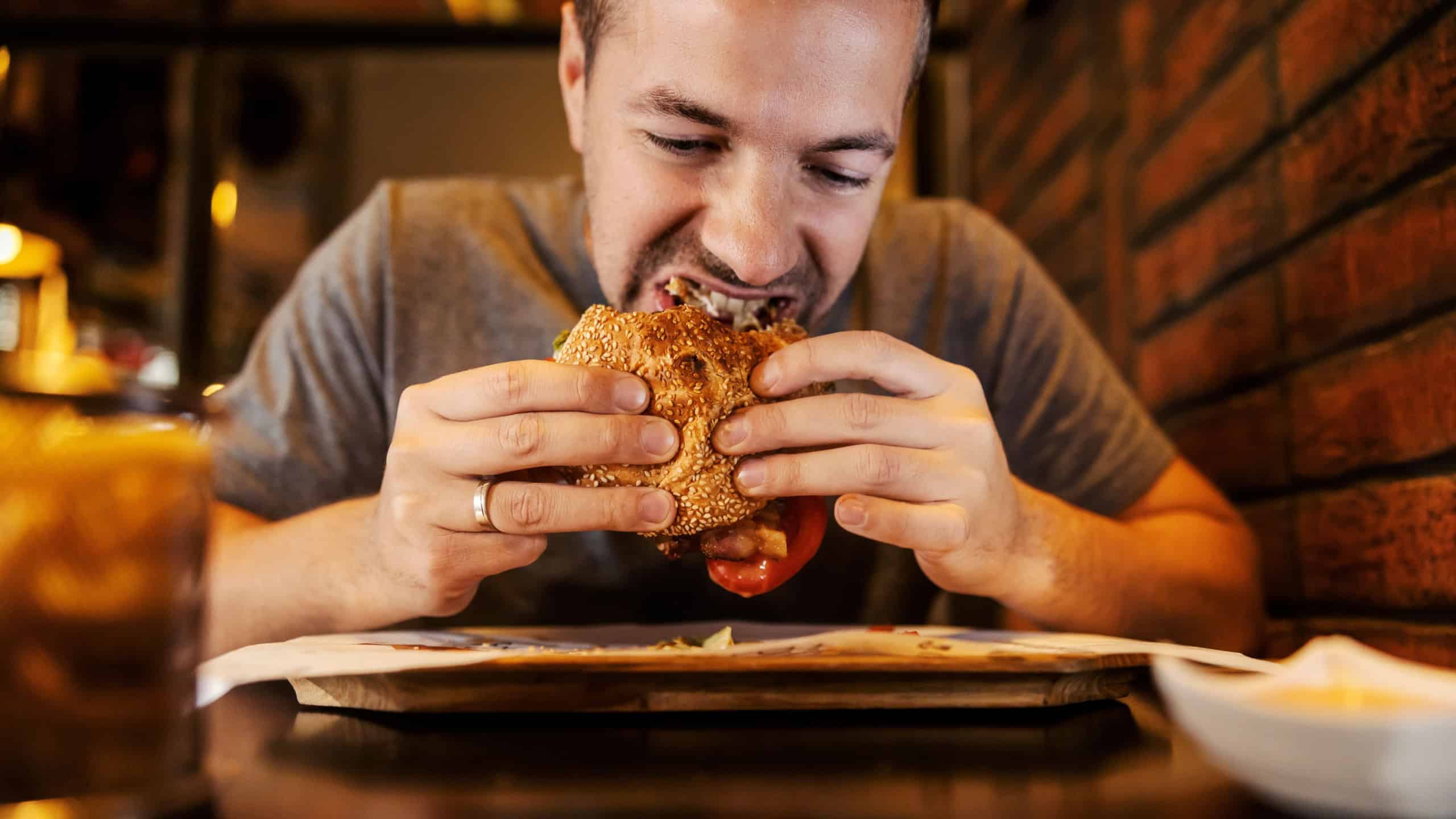 Close up of a starving man eating hamburger in a restaurant.
