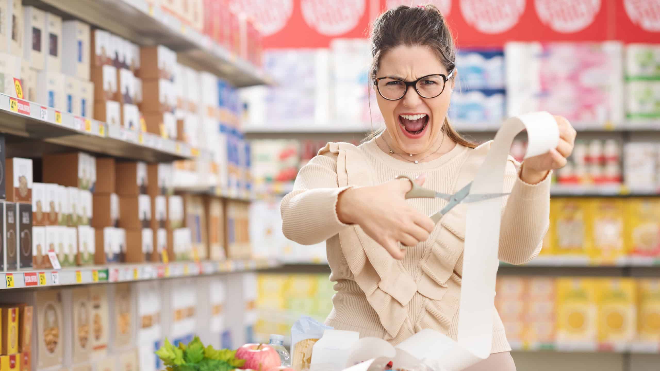 Woman doing grocery shopping at the supermarket, she is cutting a long grocery receipt: cut-price, discounts and affordable grocery concept