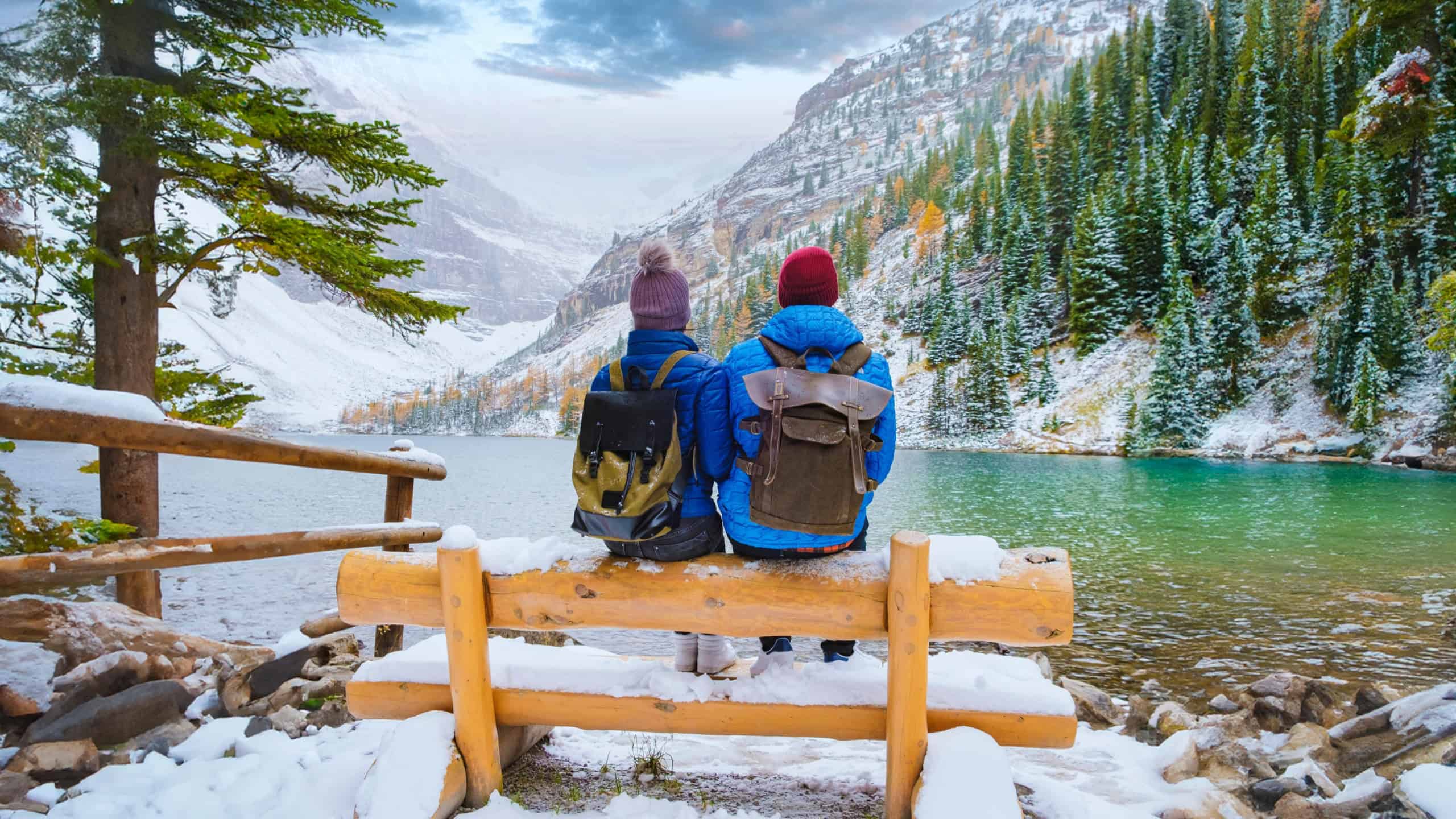 Lake Agnes by Lake Louise Banff National Park with snowy mountains in the Canadian Rocky Mountains during winter. A couple of men and women sitting on a bench by the emerald green lake in Canada 