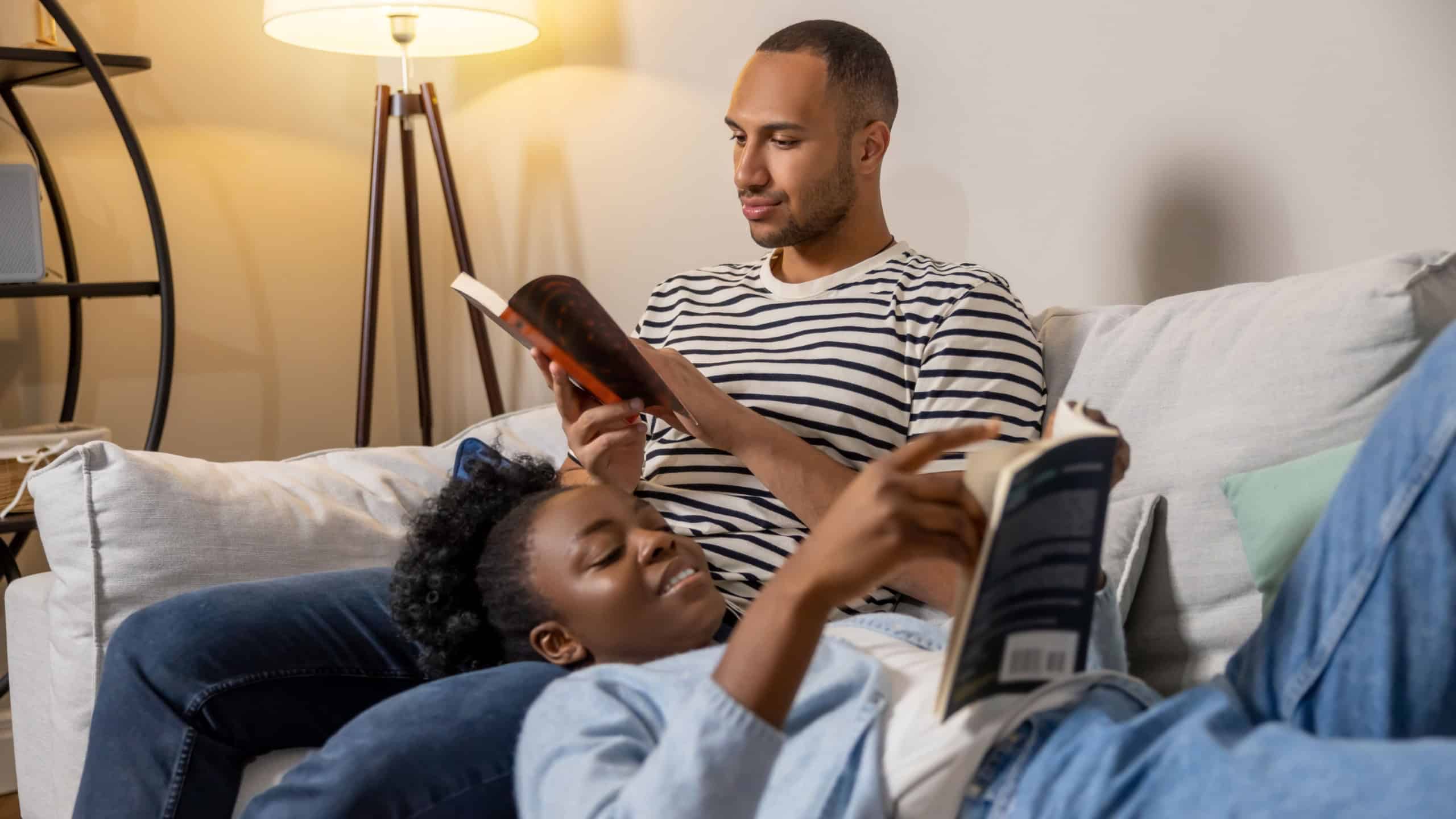 Couple reading books while resting on sofa together at home