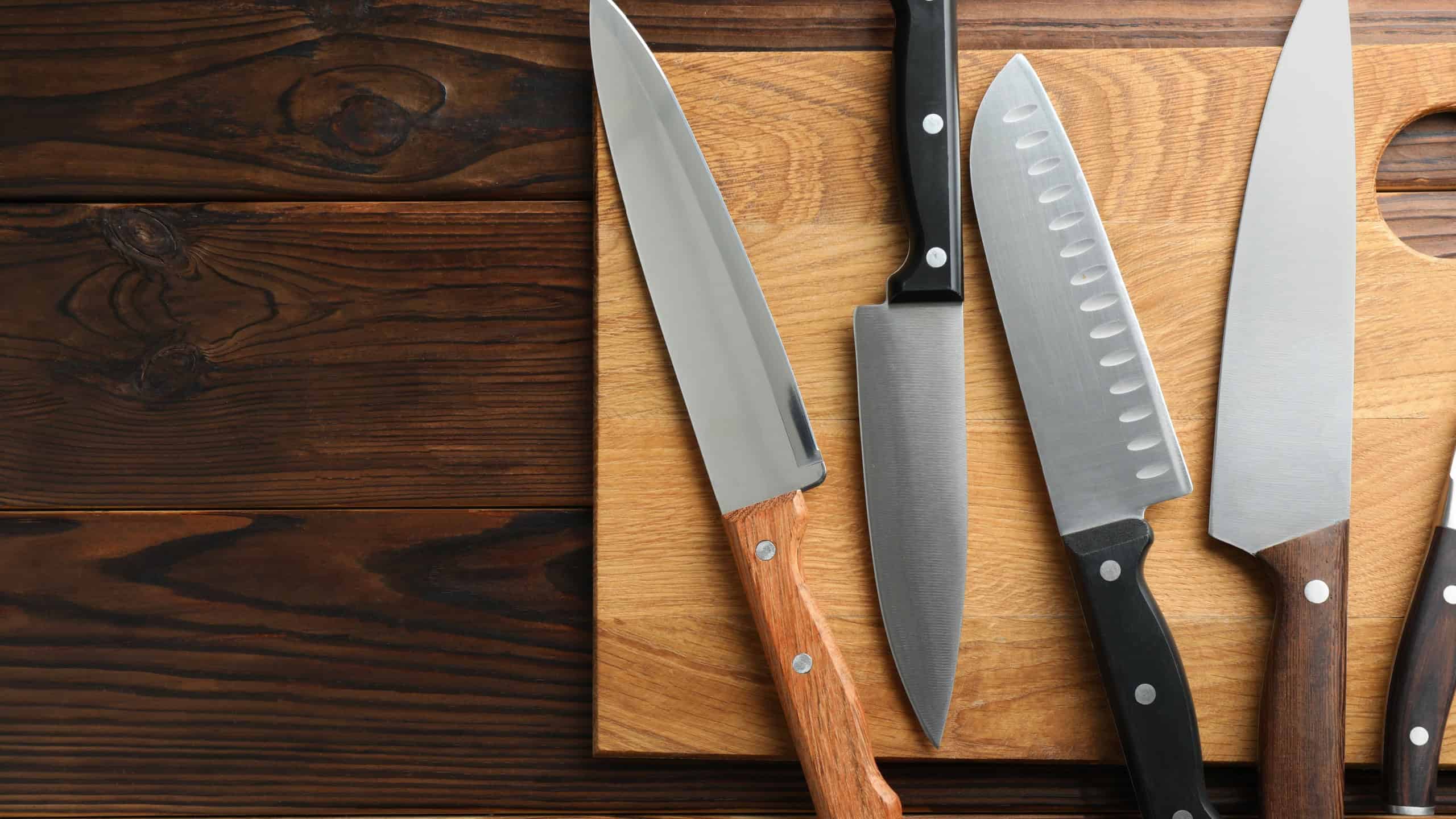 Many different knives and board on wooden table, top view. Space for text
