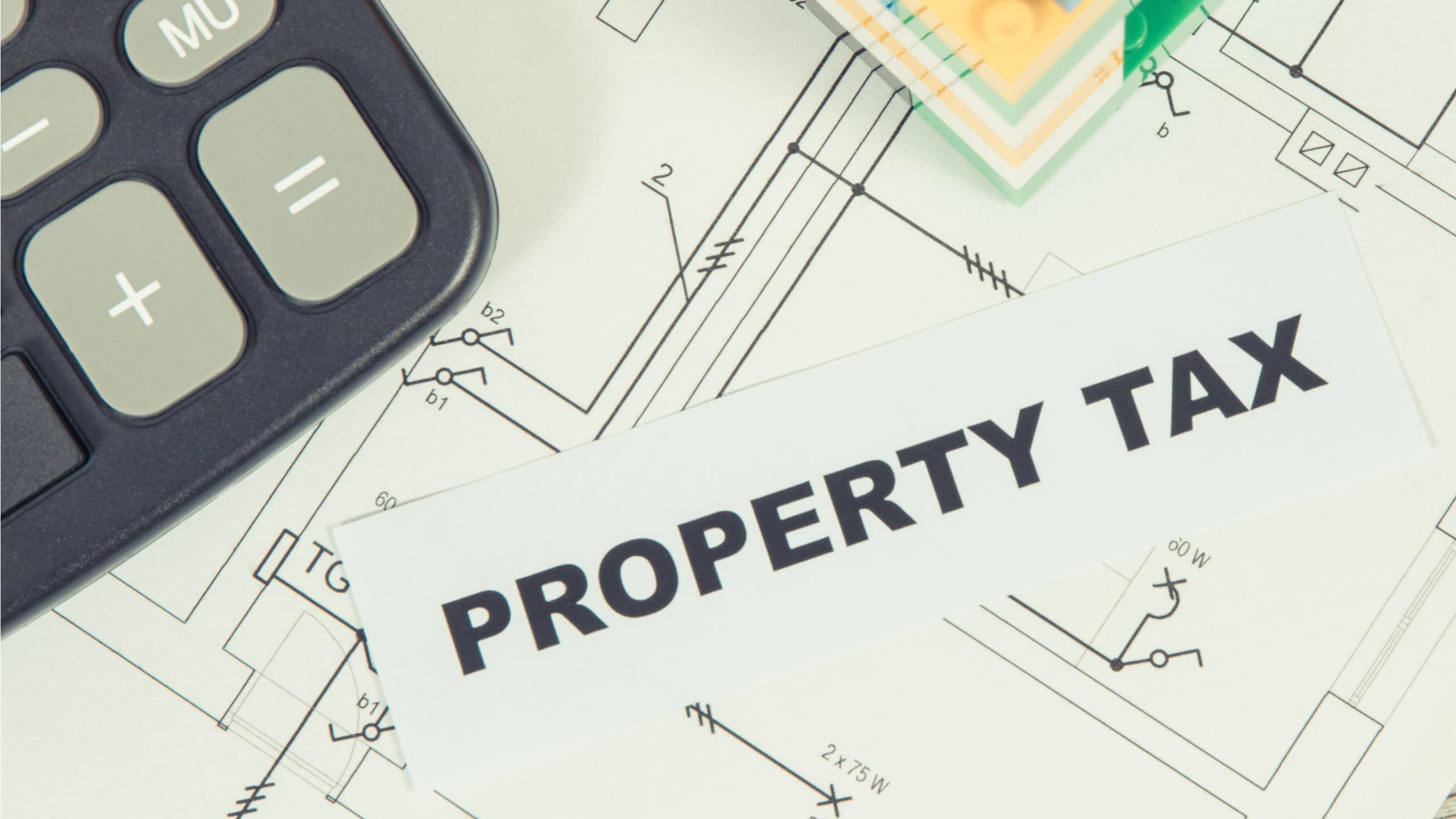 Inscription property tax with small house made of colorful toy blocks and calculator. Increasing real estate or luxury taxation. Tax payments