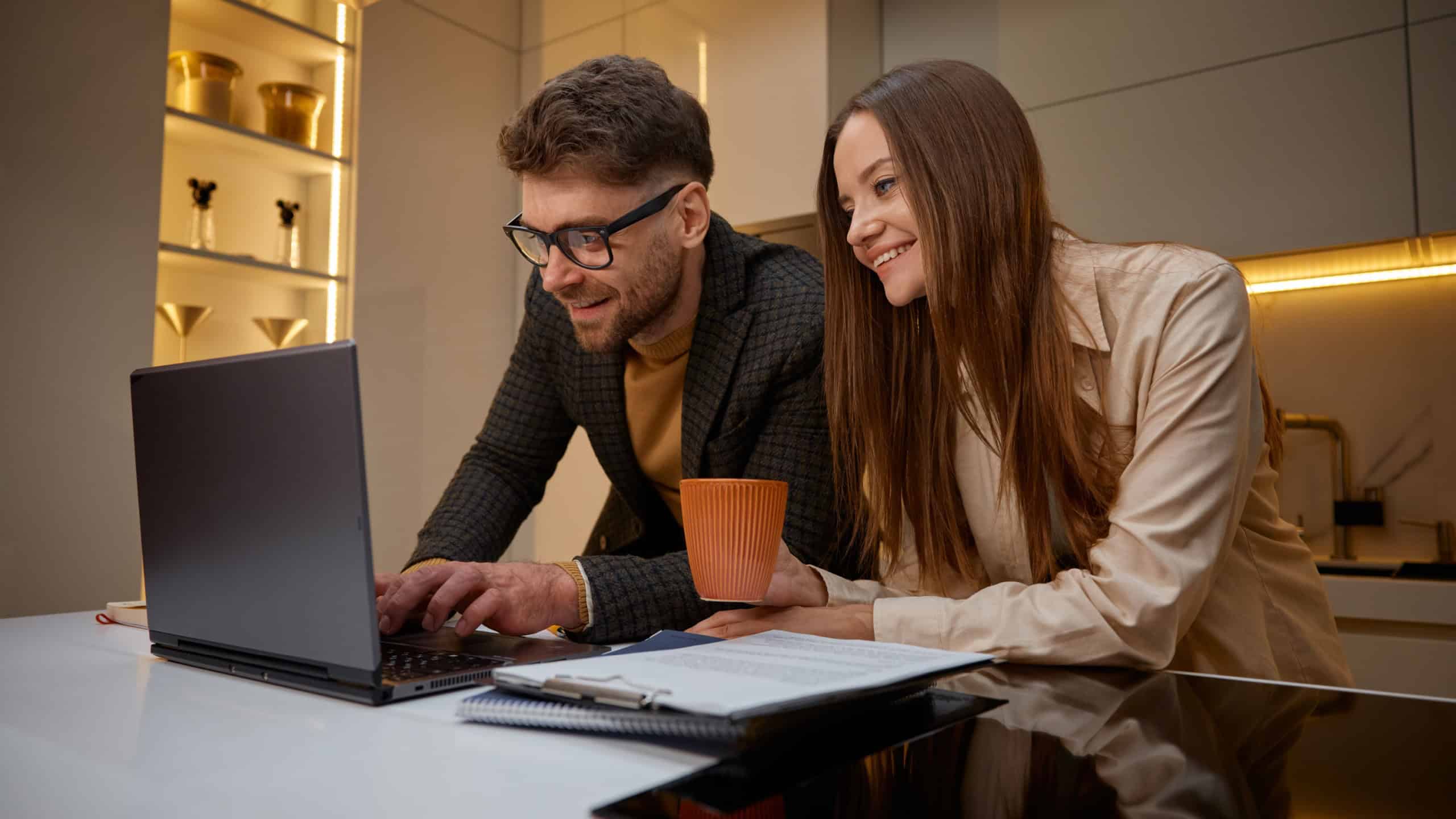 Young family using laptop on kitchen, husband helping loving wife with project