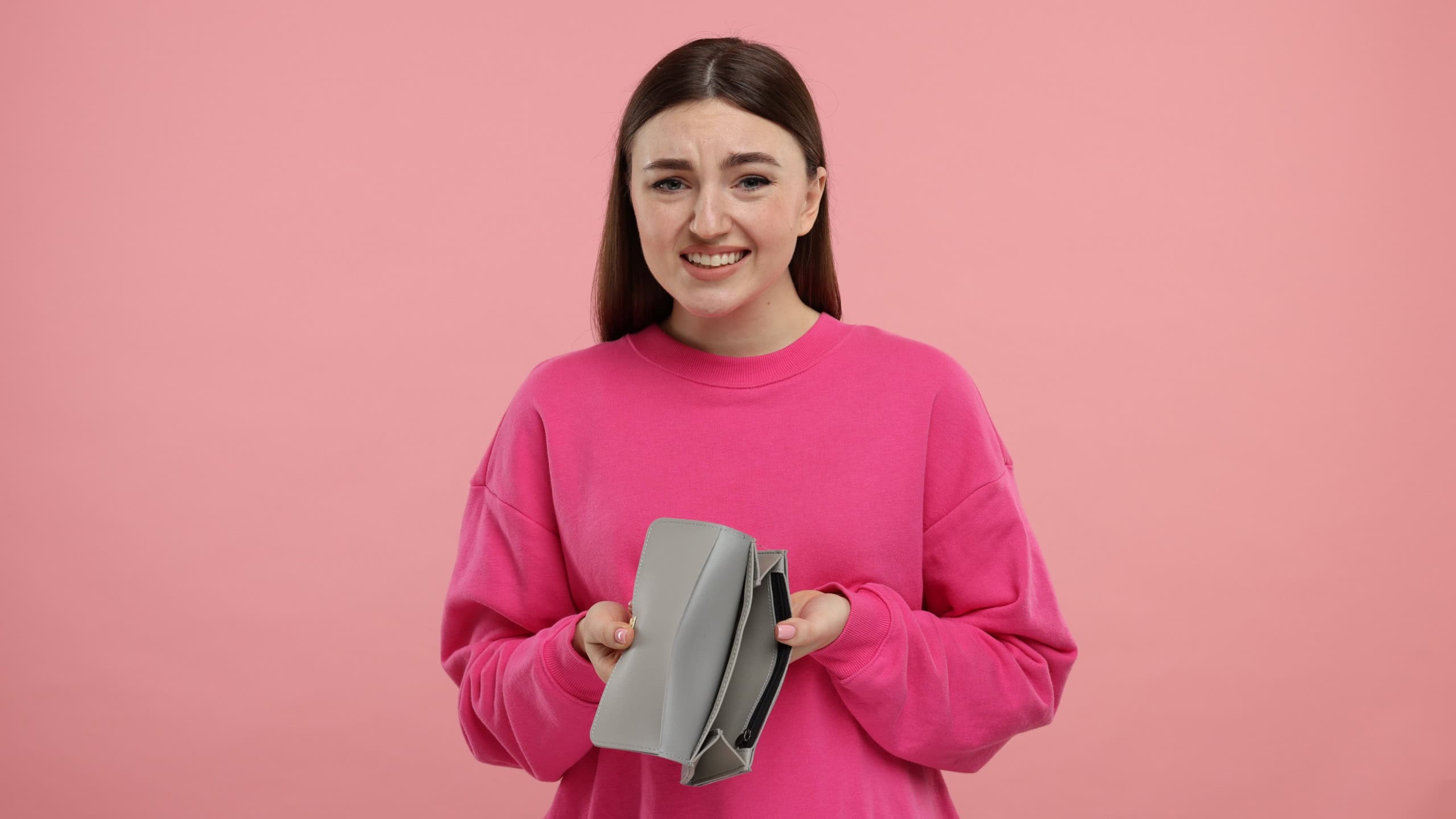 Woman showing empty wallet on pink background