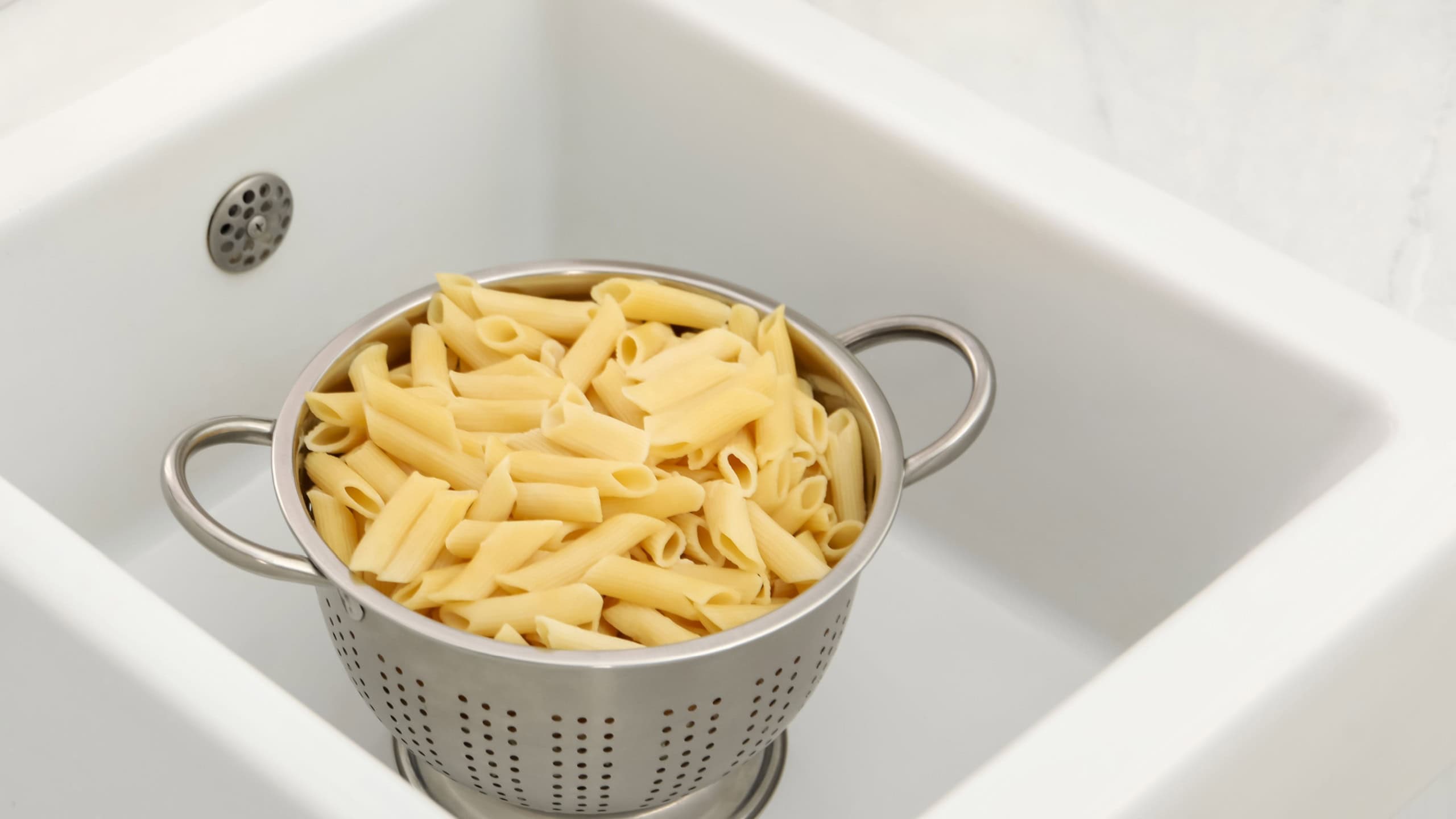 Metal colander with cooked pasta in sink