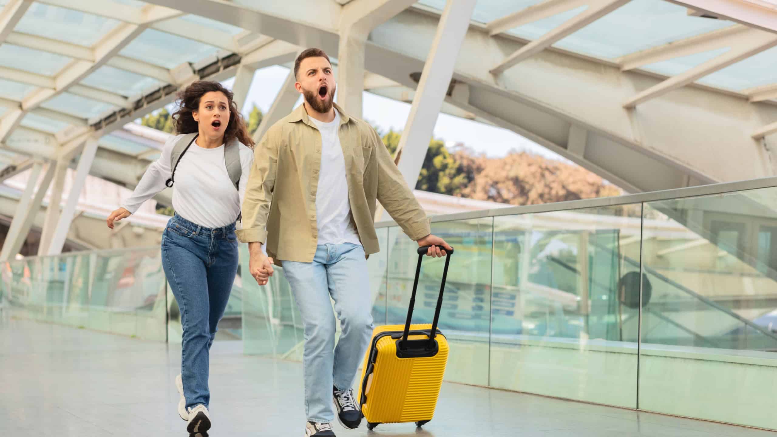 Two people in casual attire are running with expressions of panic, possibly late for a flight, in an architecturally modern airport with a yellow suitcase