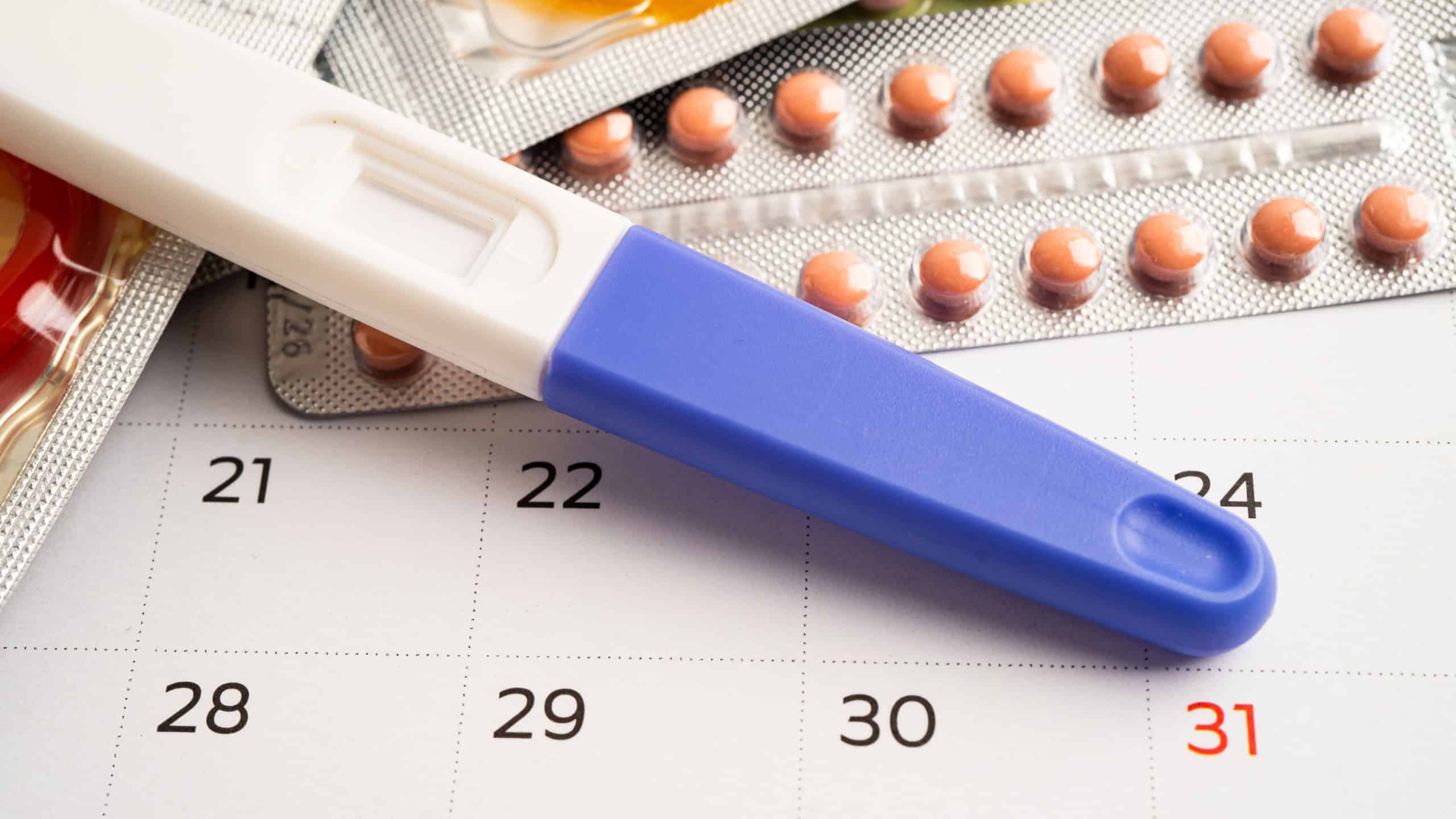 Pregnancy test and birth control pills on calendar, contraception health and medicine.