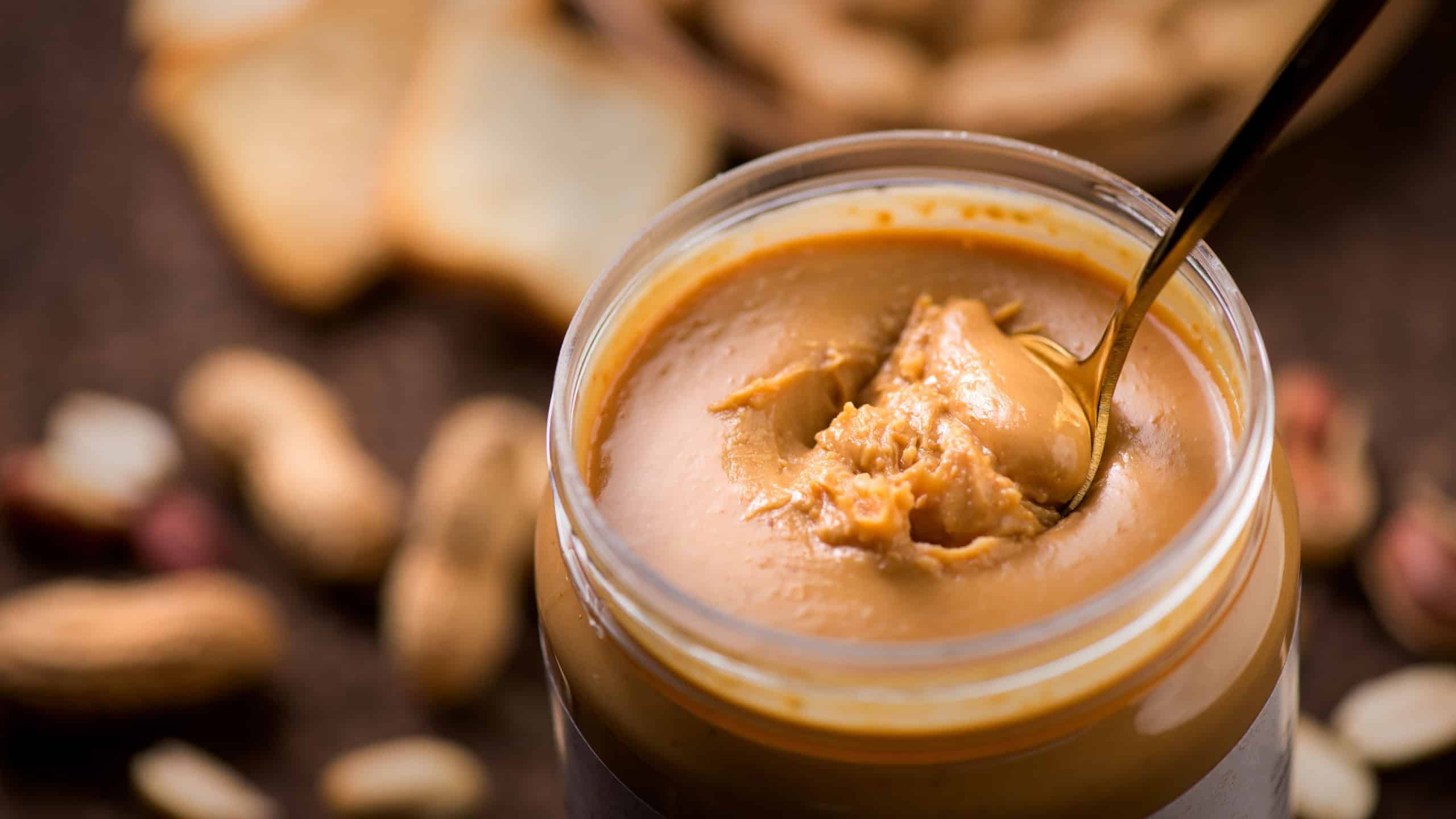 Peanut butter. Creamy smooth peanut butter in jar on a table. Spoon of natural organic vegan food. American cuisine. 