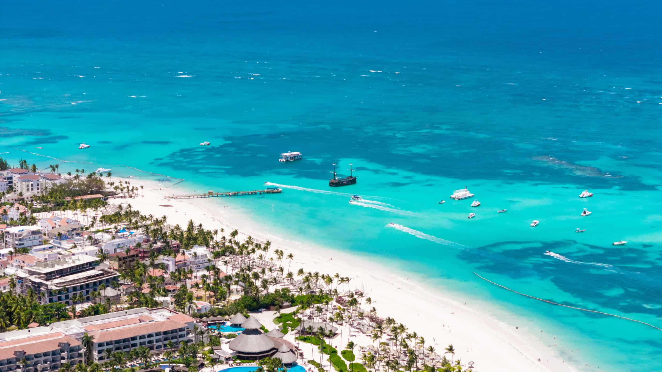 Aerial view of beautiful tropical white sand Los Corales beach in Punta Cana. Moored pirate ship in turquoise Caribbean sea water. Best attractions and excursions in Dominican Republic 