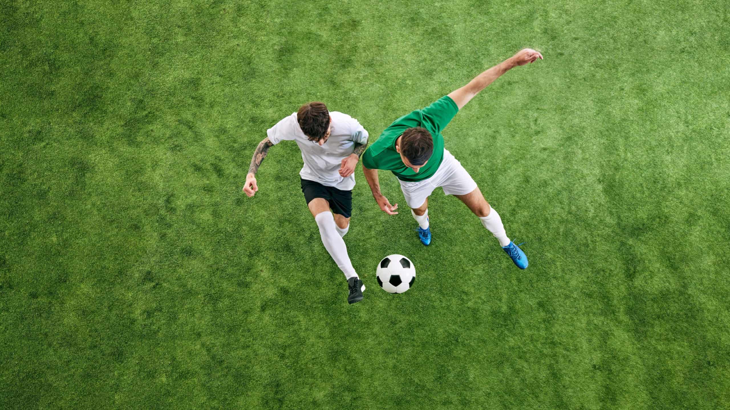 Aerial view. Two male soccer players compete for possession of ball on green lush playground. Concept of professional sport, championship, tournament, final match, movement. Ad
