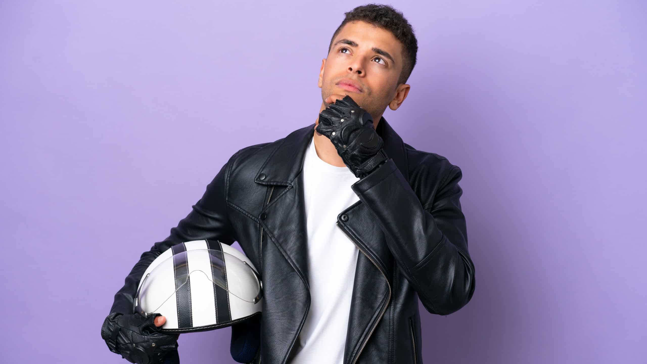 Young Brazilian man with a motorcycle helmet isolated on purple background and looking up