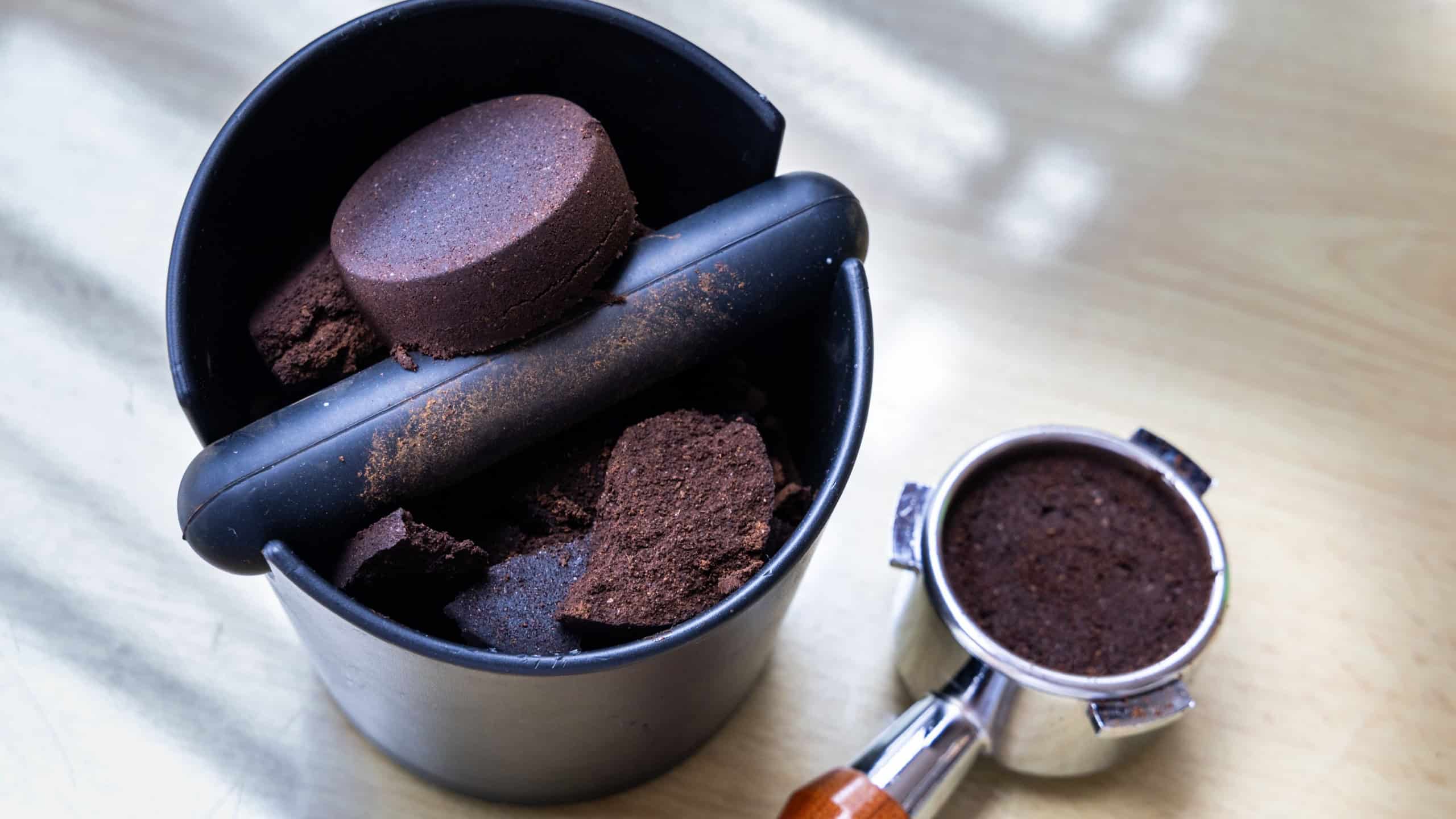 Compacted coffee ground in knock box with portafilter next to it. Coffee grounds are excellent natural and organic fertilizers.