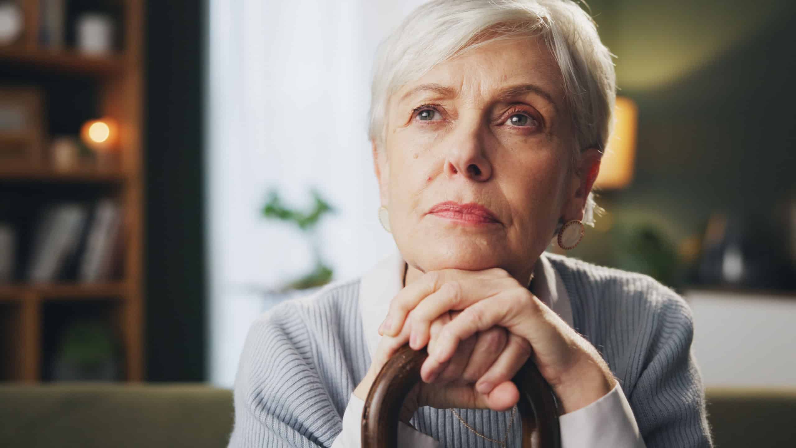 Walking stick, memory and senior woman in home with thinking, remember or nostalgia for past. Dreaming, medical support and elderly female person with cane for dementia disease in retirement facility