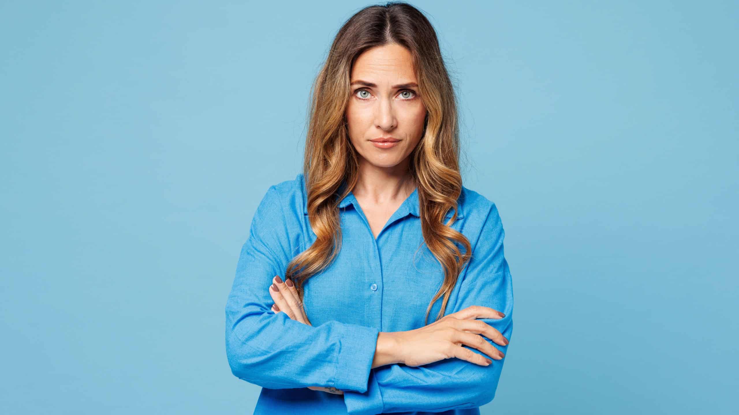 Young frowning indignant sad mad woman she wearing shirt casual clothes hold hands crossed folded looking camera isolated on plain pastel light blue cyan background studio portrait. Lifestyle concept