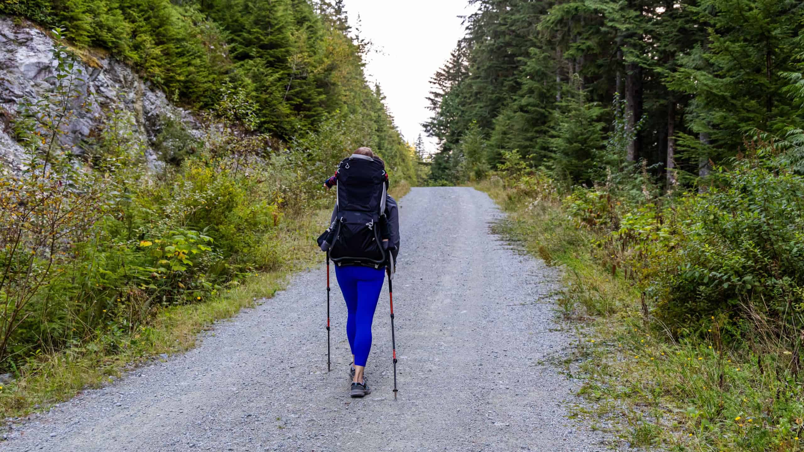 A woman hikes on a tranquil forest trail in Mission, BC, Canada, surrounded by lush greenery and mountains. Experience the peacefulness of nature and outdoor adventure.