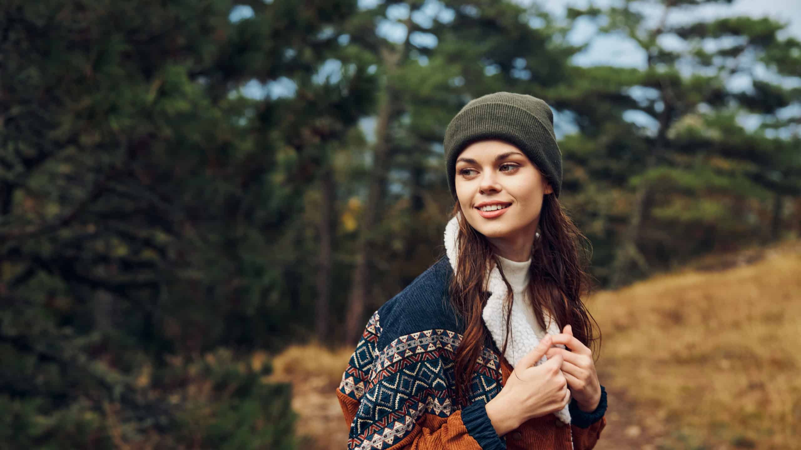A woman enjoying a peaceful moment in nature, surrounded by trees on a hill in cozy sweater and beanie