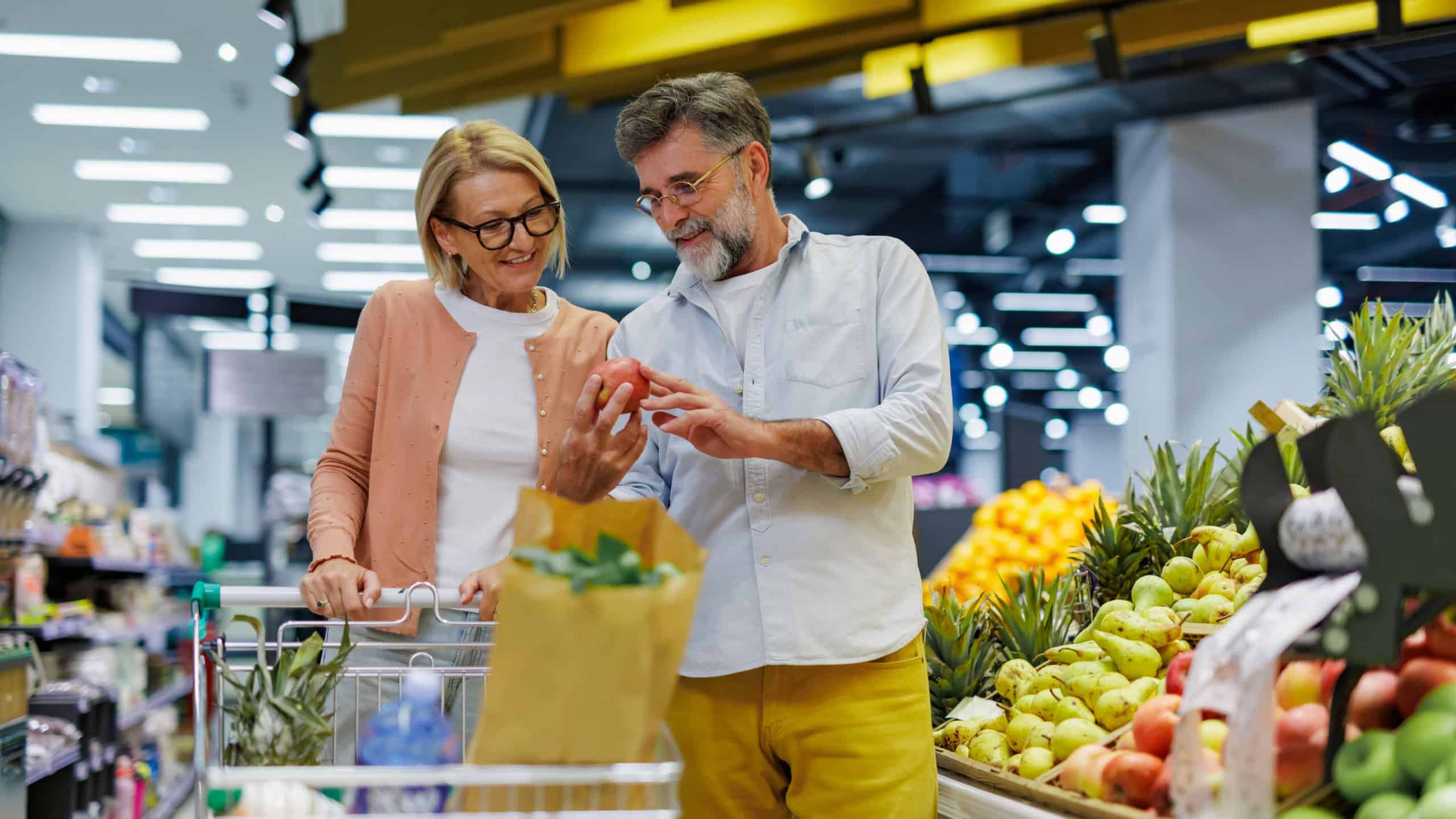Cheerful senior couple happily picks fresh fruits in a supermarket, embodying a healthy lifestyle and love for nutritious food