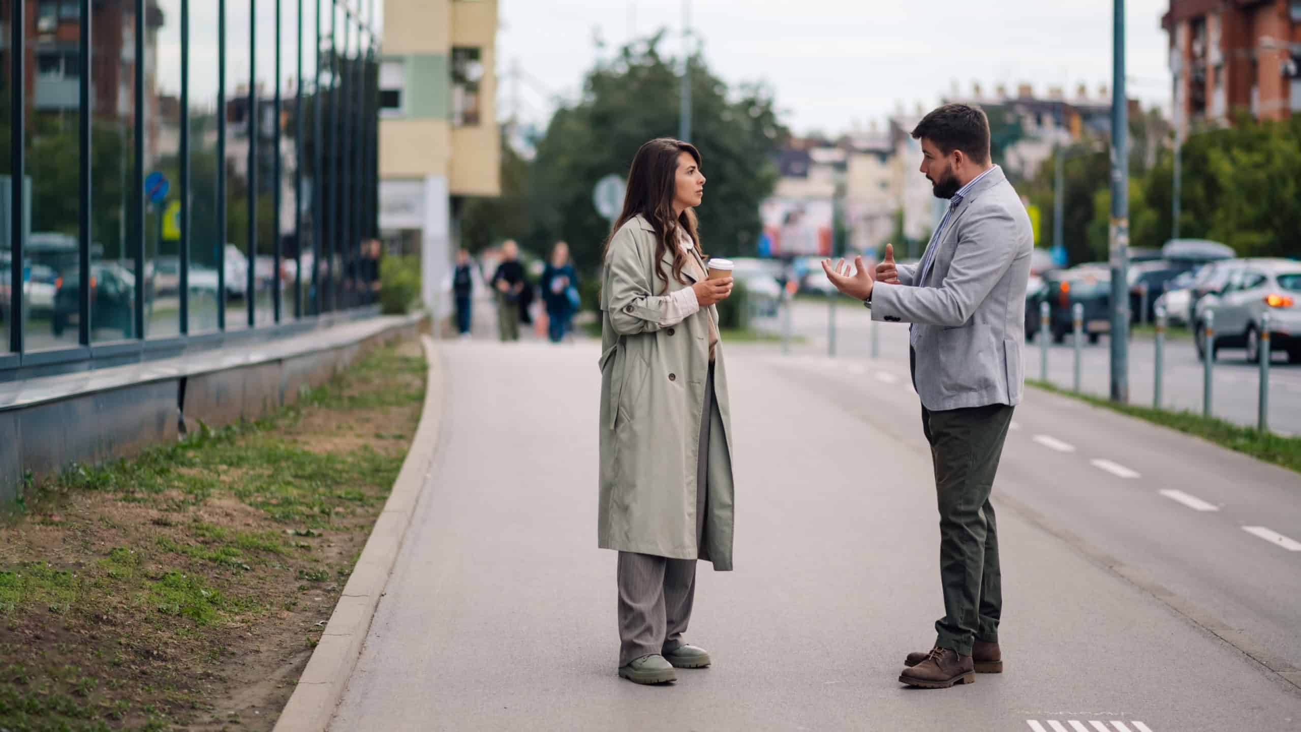 Two coworkers are discussing work matters on a city street during their coffee break, engaged in a lively exchange of ideas and perspectives