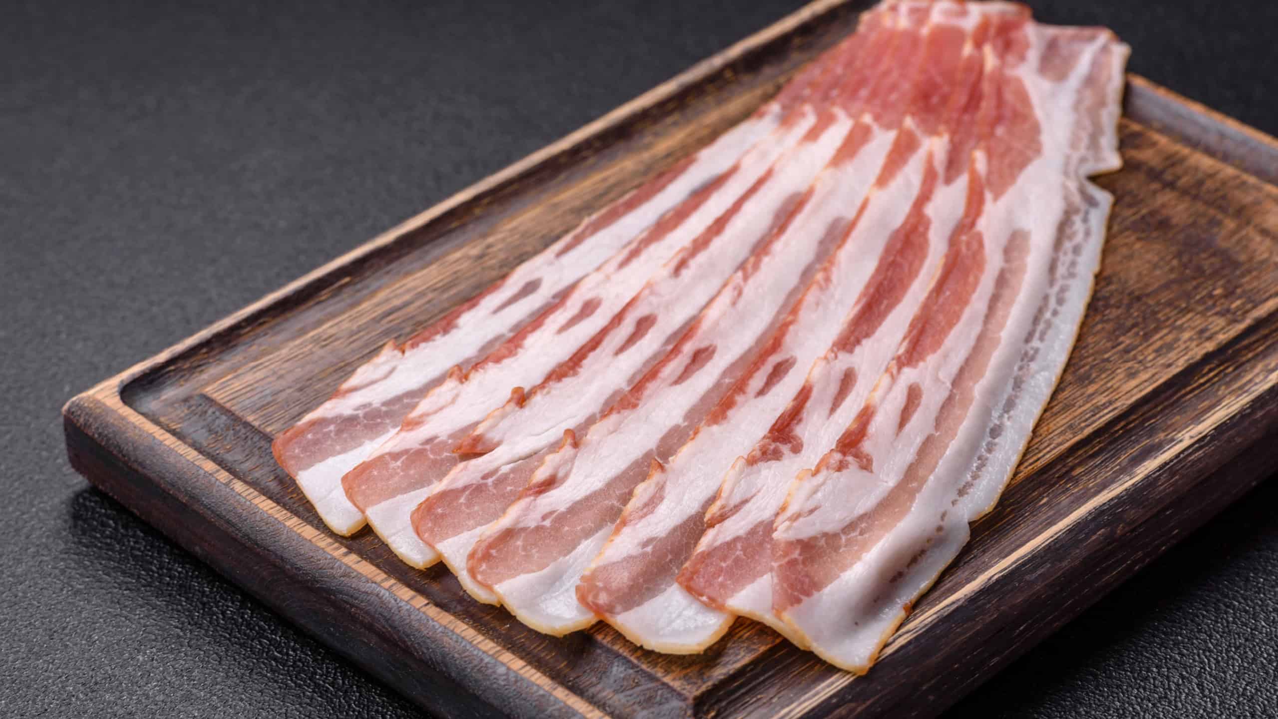 Fresh raw bacon sliced with spices and herbs on a dark concrete background