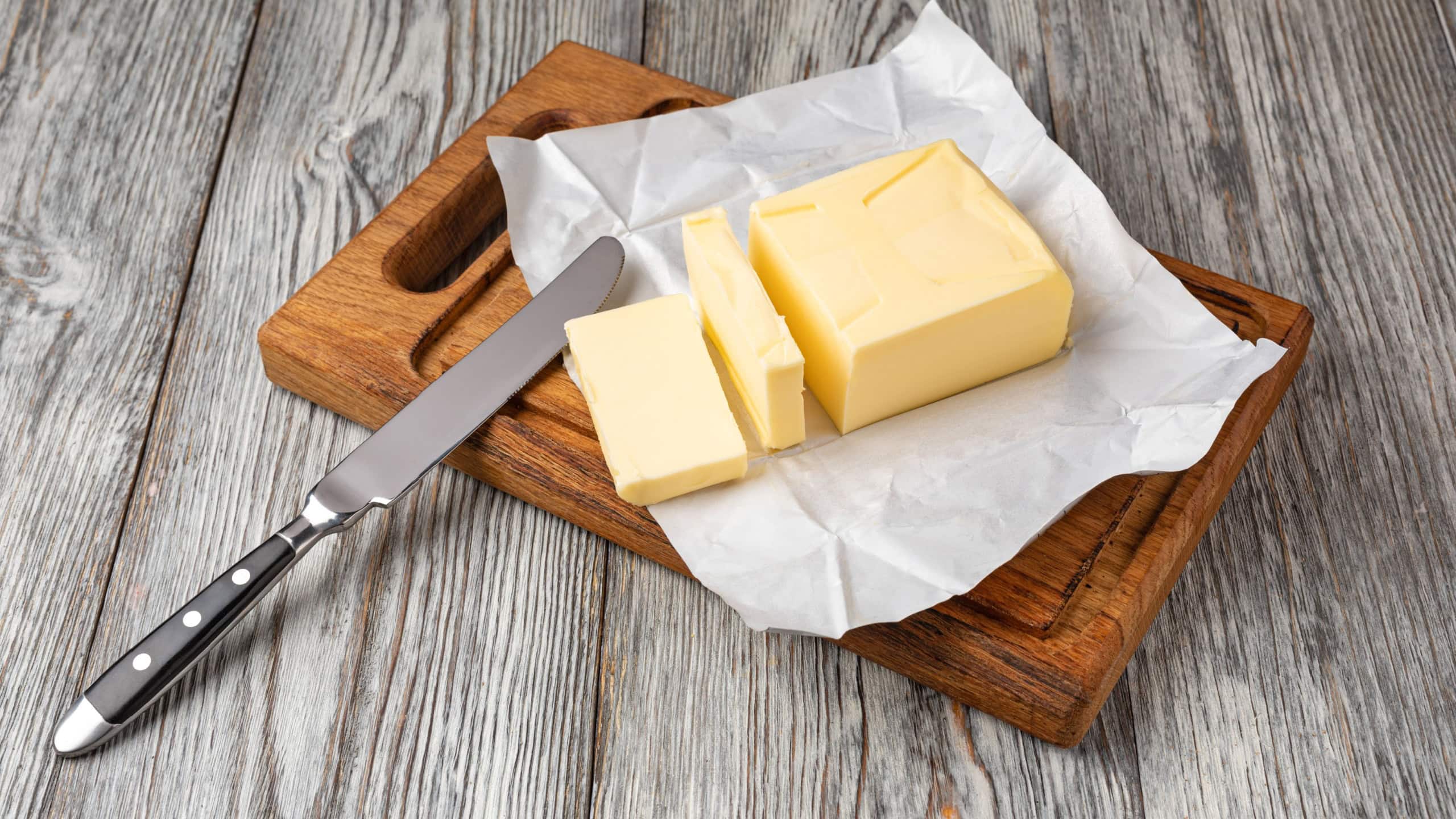 Fresh butter slices on a wooden cutting board with a butter knife, ready for spreading