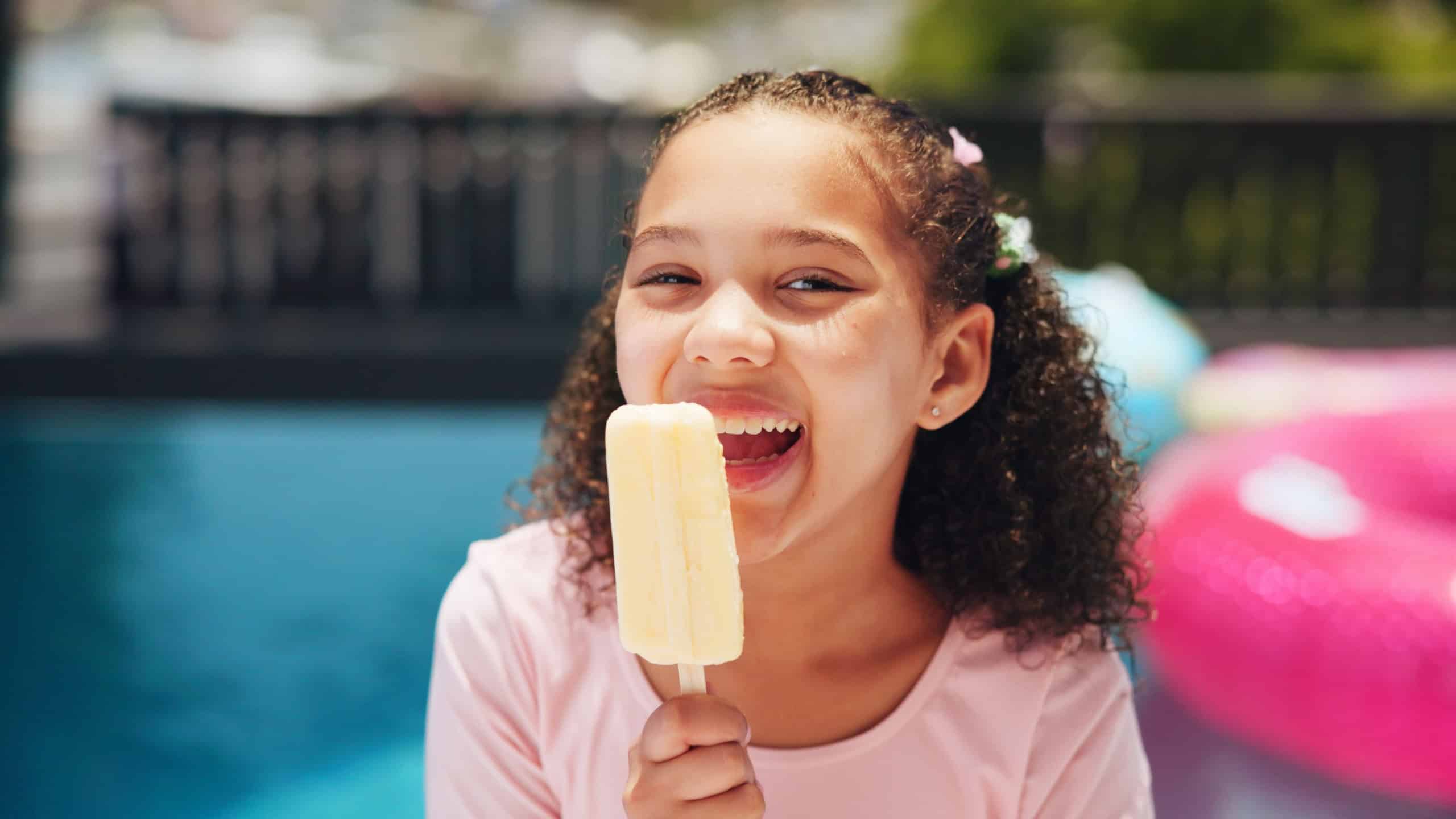 Happy girl, portrait or pool with popsicle for summer treat, holiday or vacation at luxury resort. Female person, child or kid eating with smile, dessert or ice cream for sweet or cold snack at house