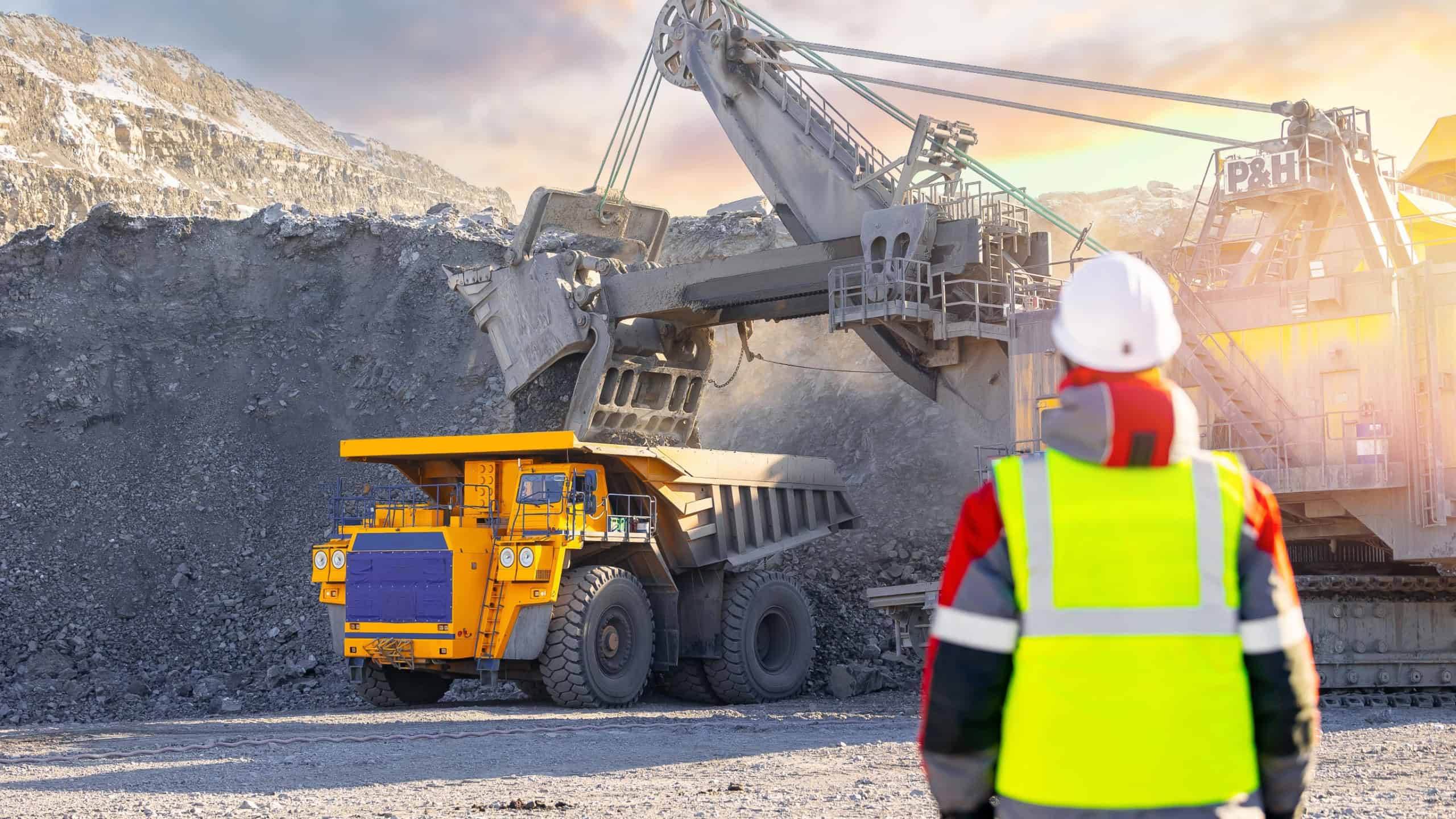 Winter coal mining operation with machinery and worker in high visibility clothing.