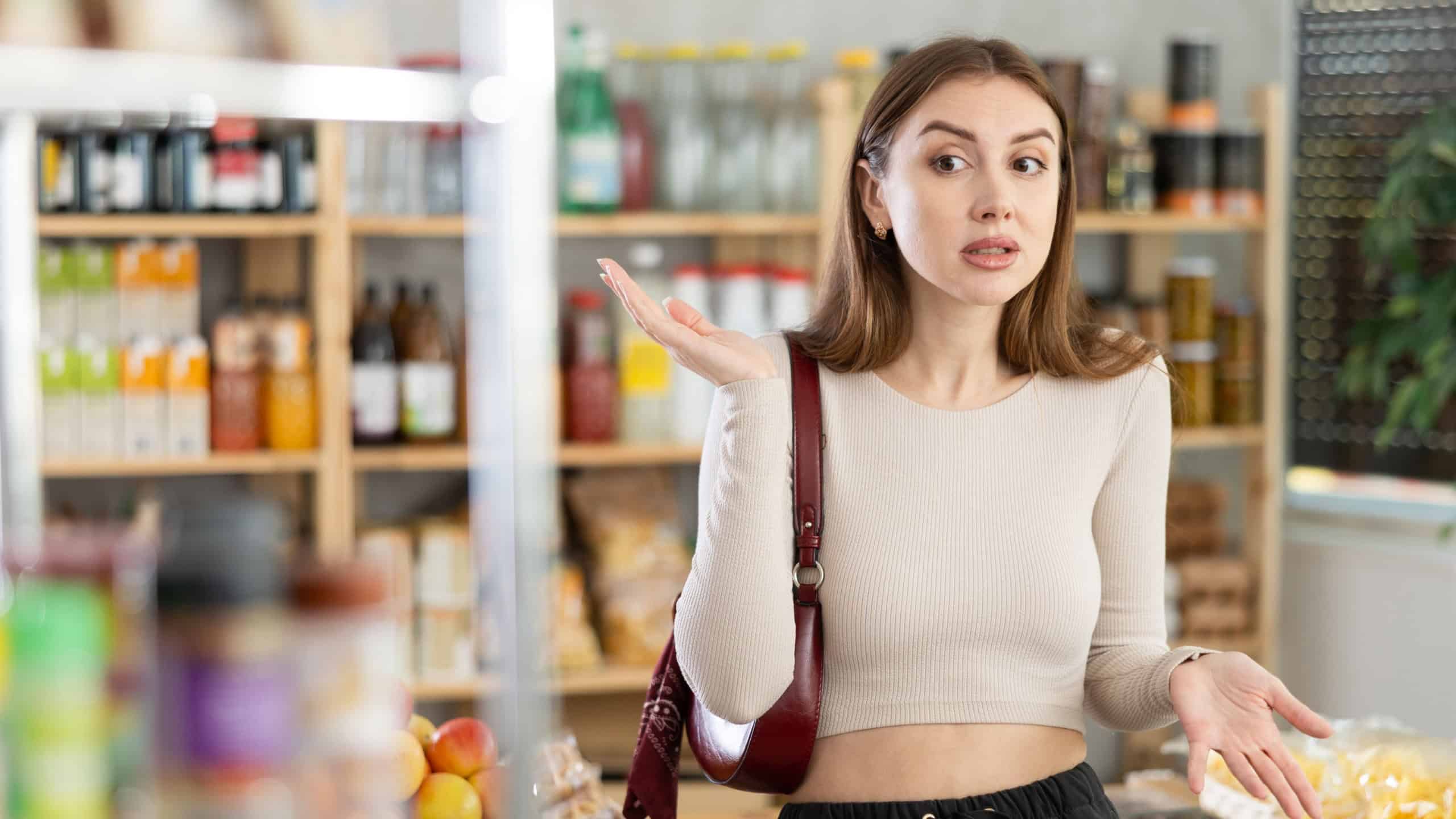 Girl customer suffers from forgetfulness, stands in store and tries to remember planned shopping list. She rubs her forehead, remembers forgotten purchase item
