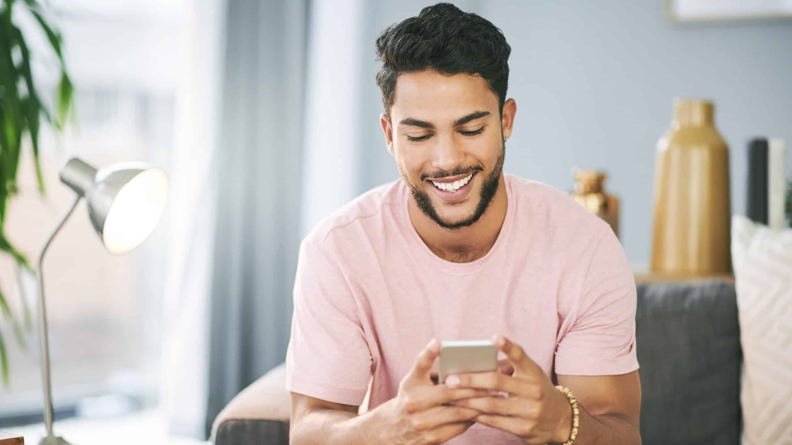 House, smile and man on sofa, cellphone and typing with social media, texting and message to contact. Happy person, email and mobile user with smartphone, online reading and funny meme in living room