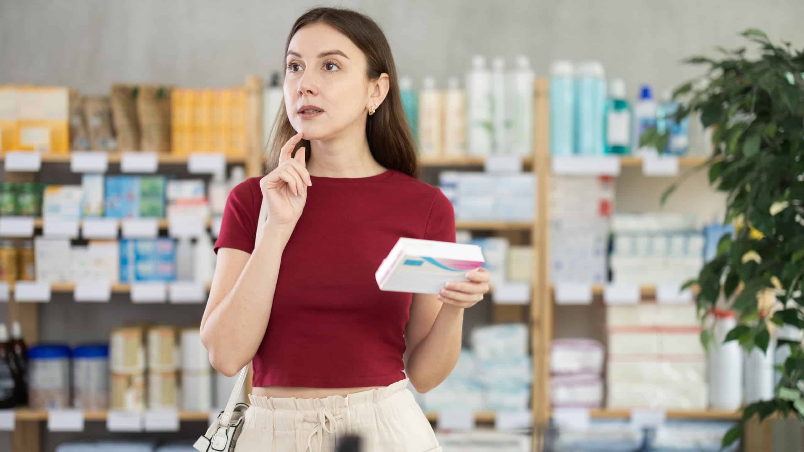 Woman choose buy paracetamol tablets box at pharmacy, compare with other good. Client check for absence of harmful substances, view product in details.