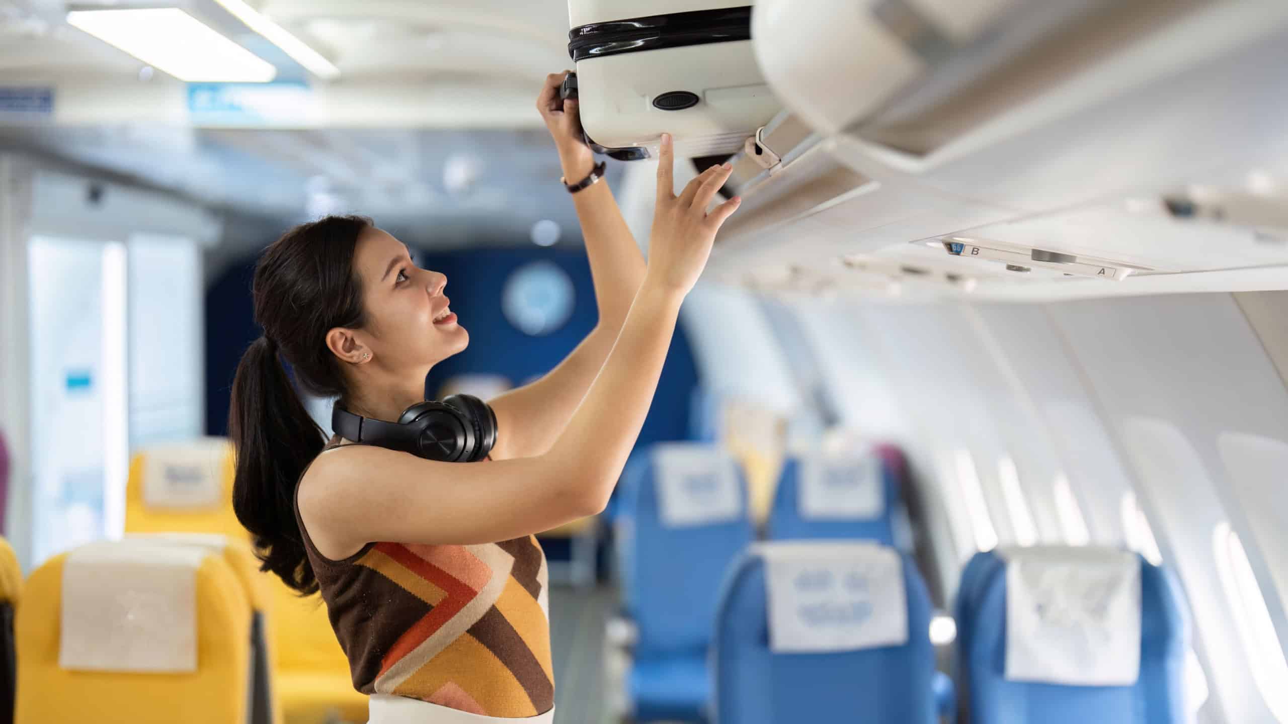 Tourist and Air Travel. A cheerful traveler managing her luggage in the airplane cabin.