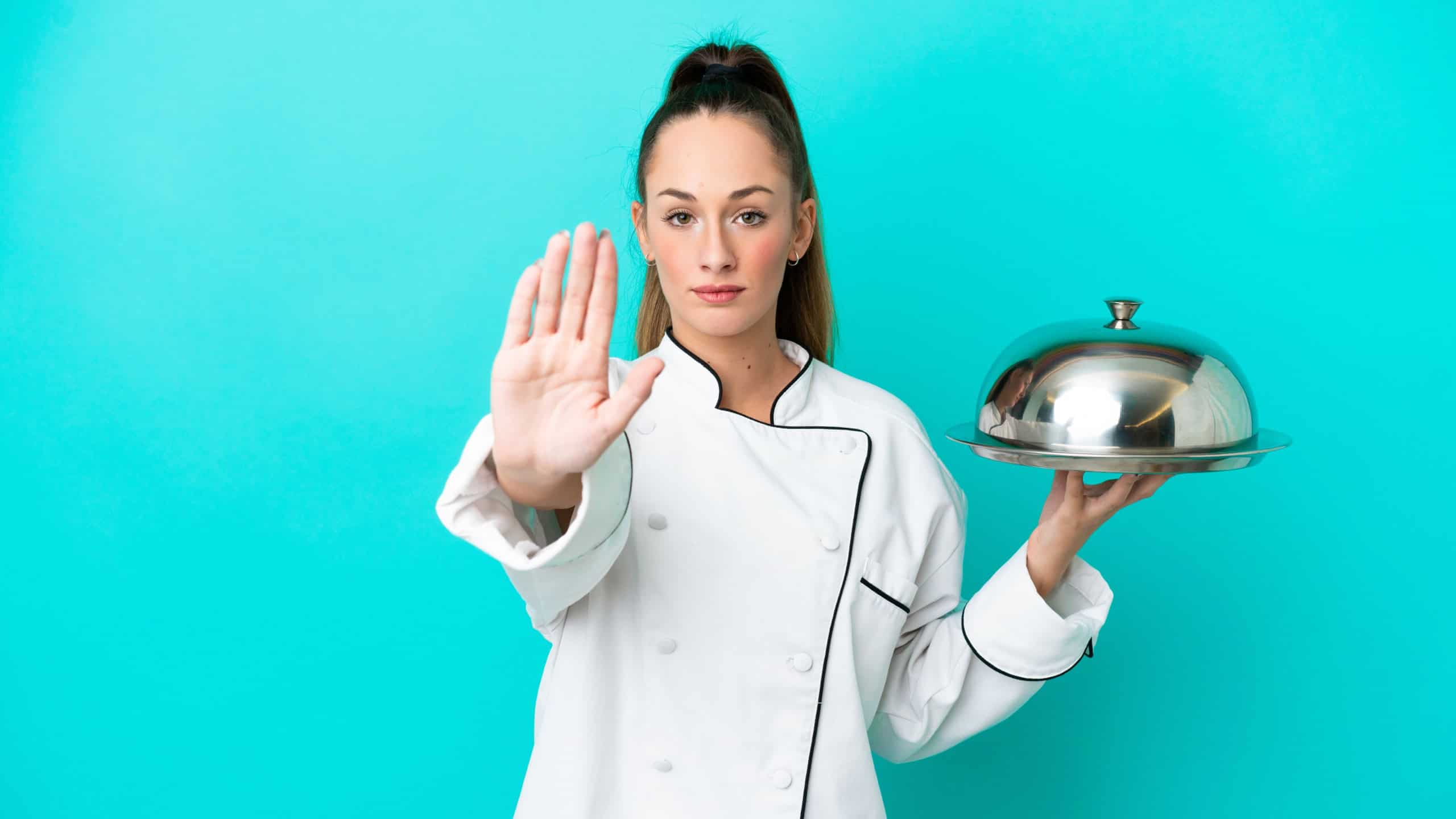 Young caucasian chef woman with tray isolated on blue background making stop gesture
