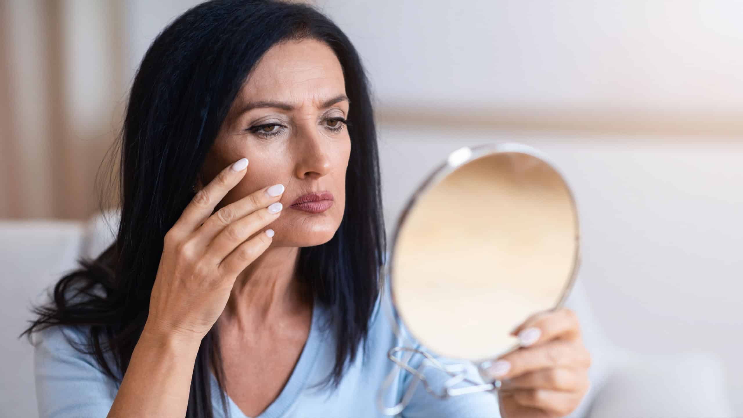 Mature woman checking her face in mirror, touching face