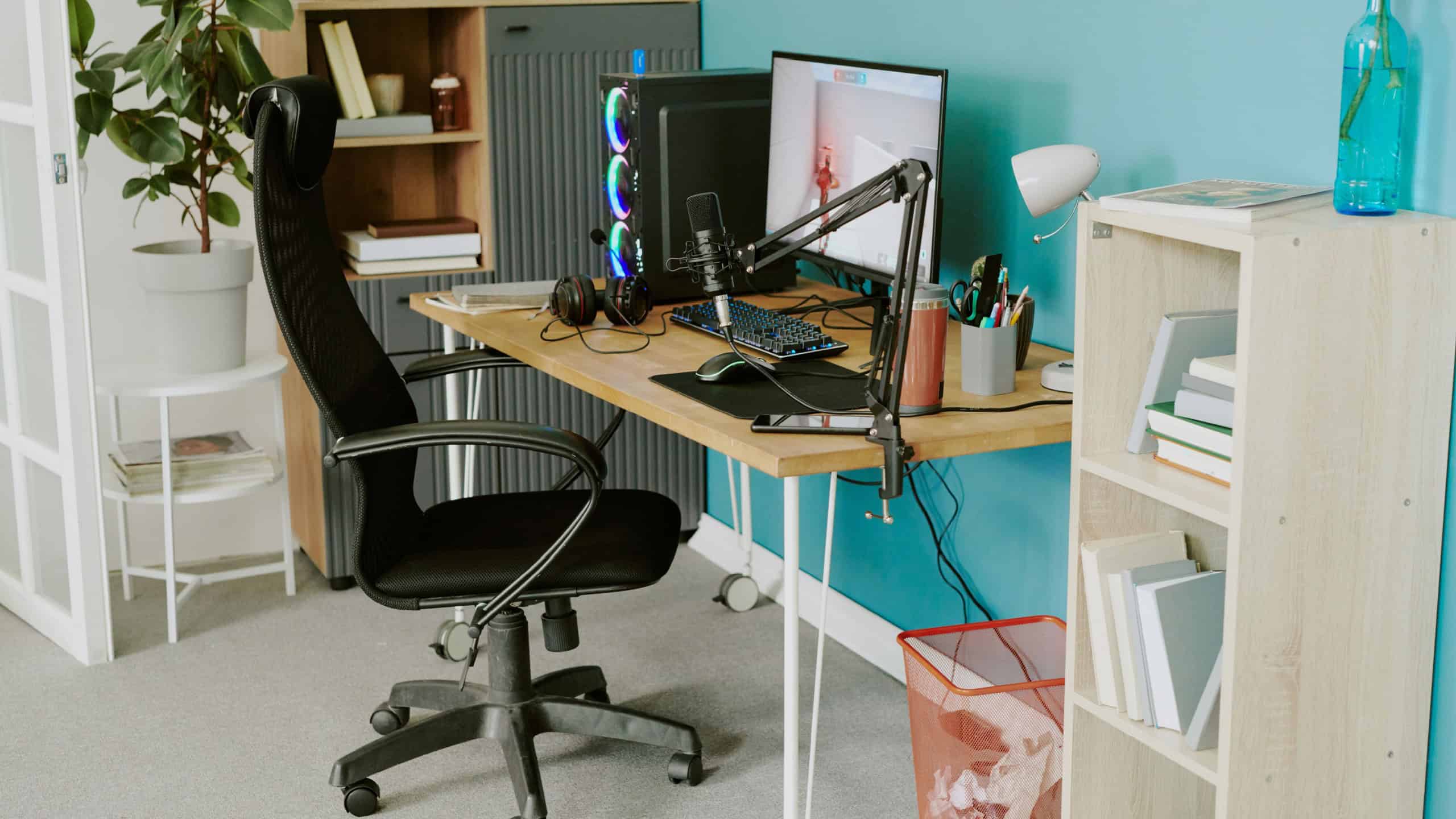 Teenager gaming setup featuring desktop computer with dual monitors, microphone, headphones, gaming keyboard, streaming equipment on desk, modern home interior visible