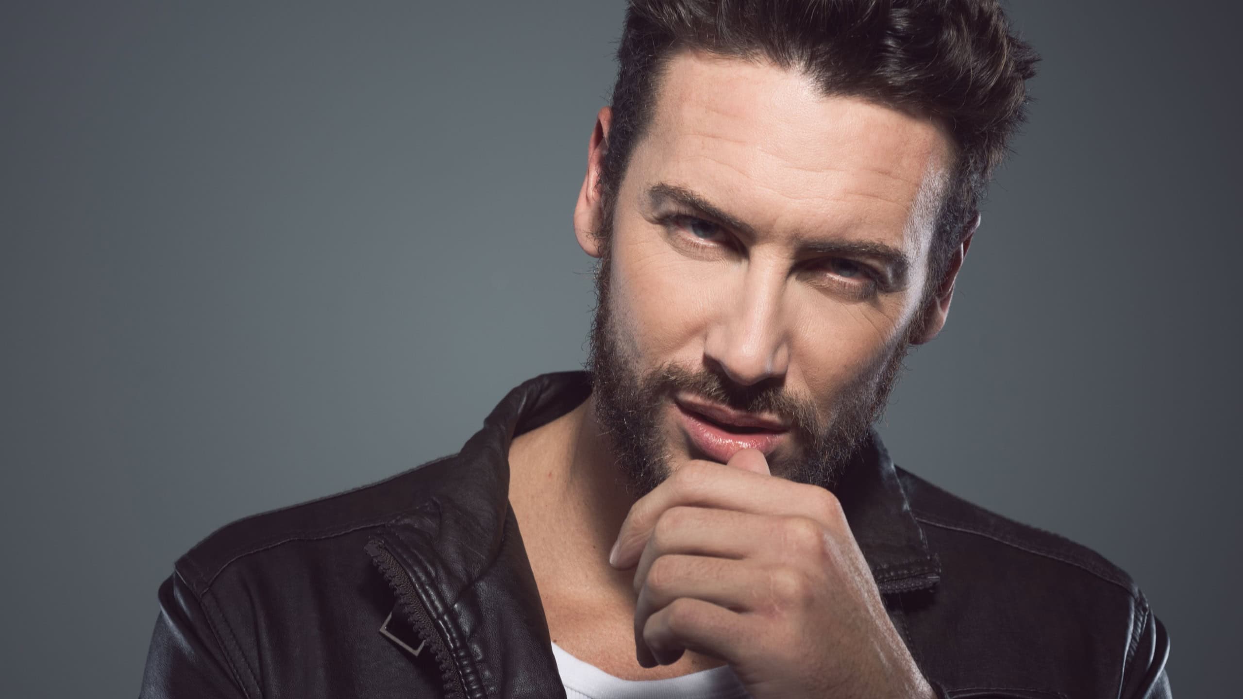 Cool seductive man in black leather jacket flirting and looking at camera