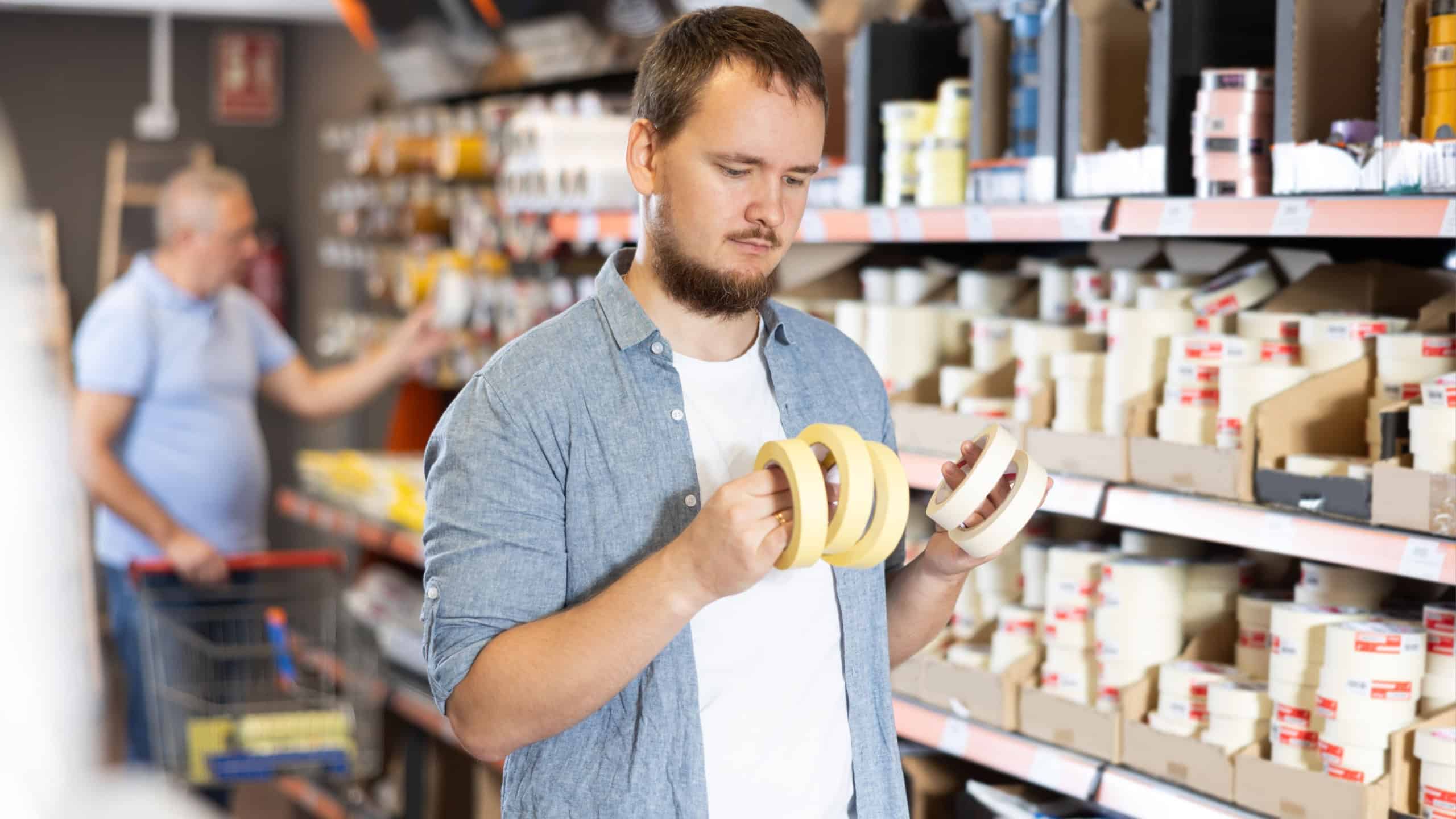 Man buys sticky adhesive tape in construction store for carrying out internal and external finishing work on object. Repair items, paint and varnish products, accessories, supermarket
