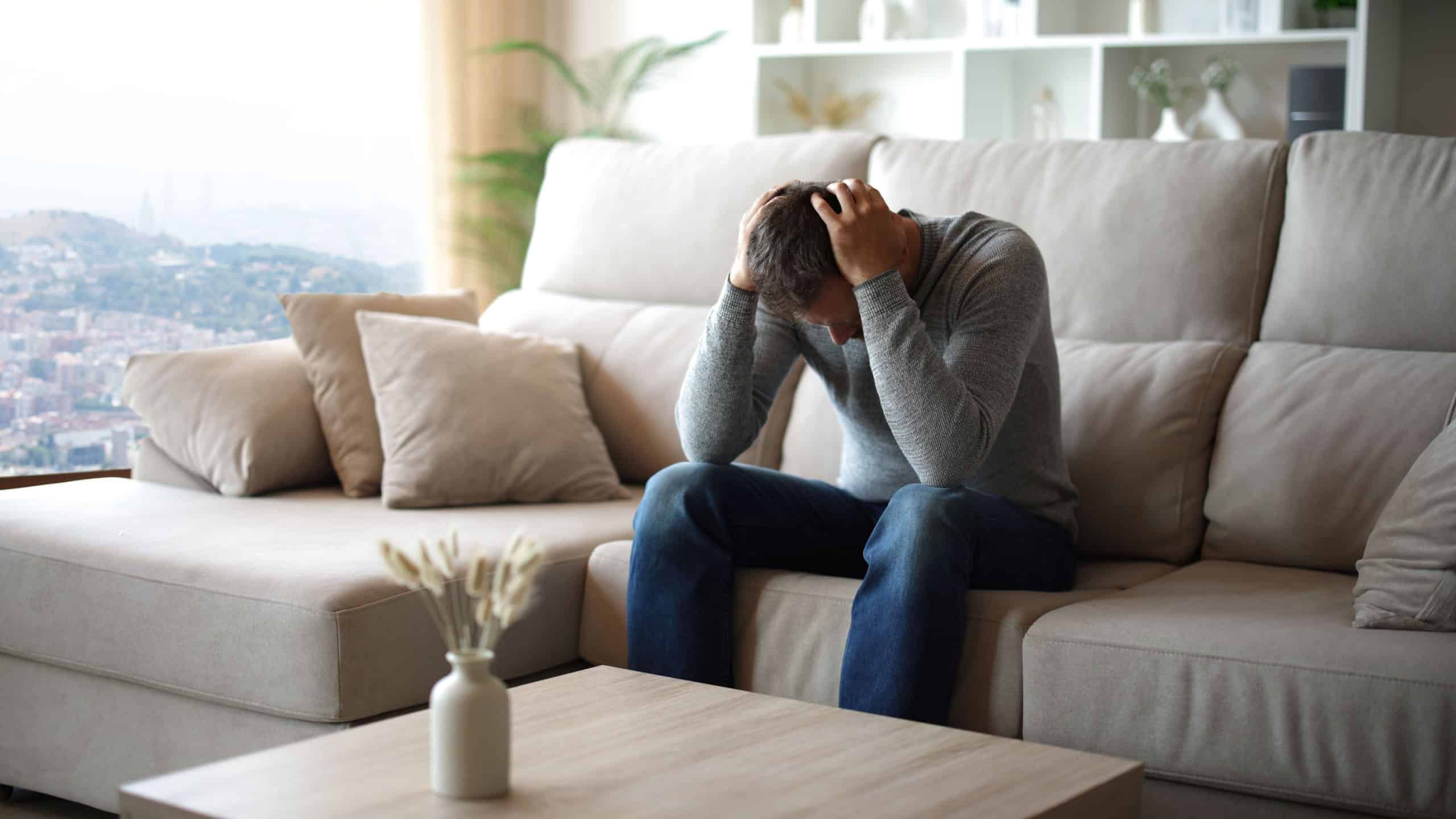 Sad man complaining alone sitting on a couch in a house interior